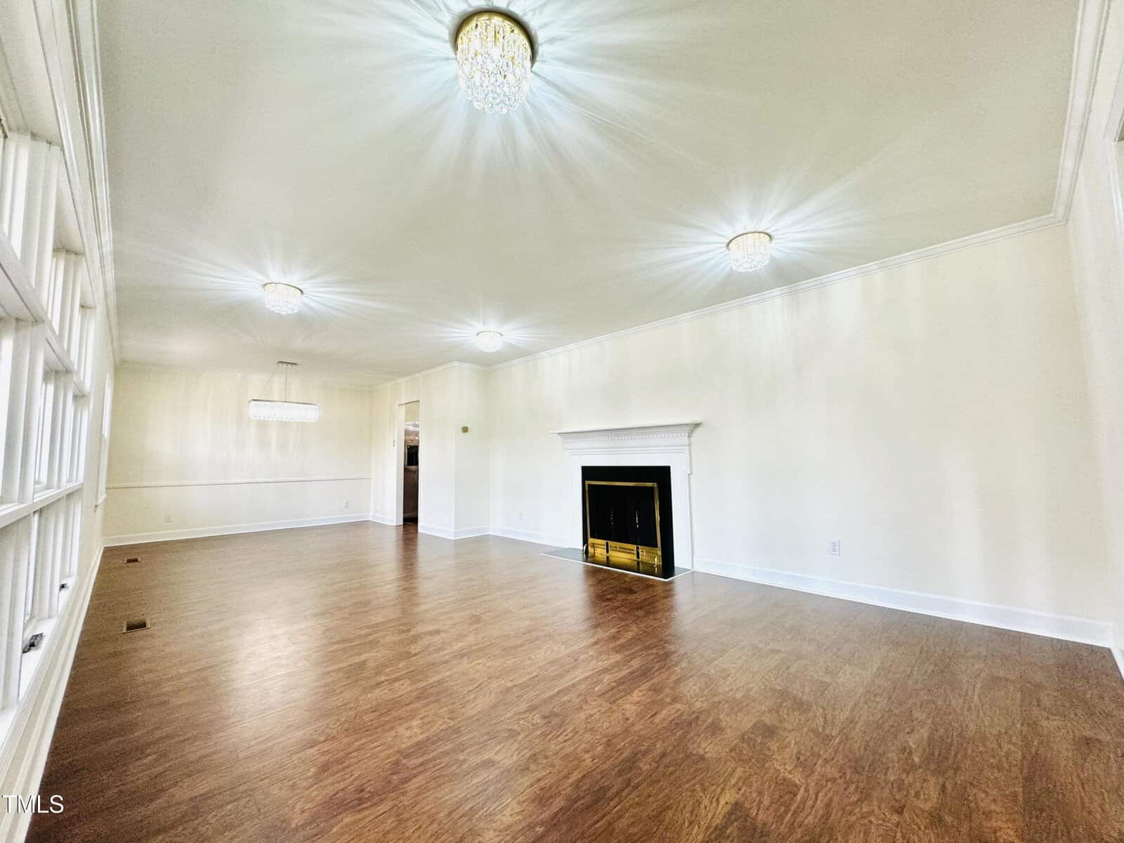 An empty room featuring glossy hardwood floors, white walls with built-in shelves, a black fireplace, and multiple ceiling lights including a chandelier.