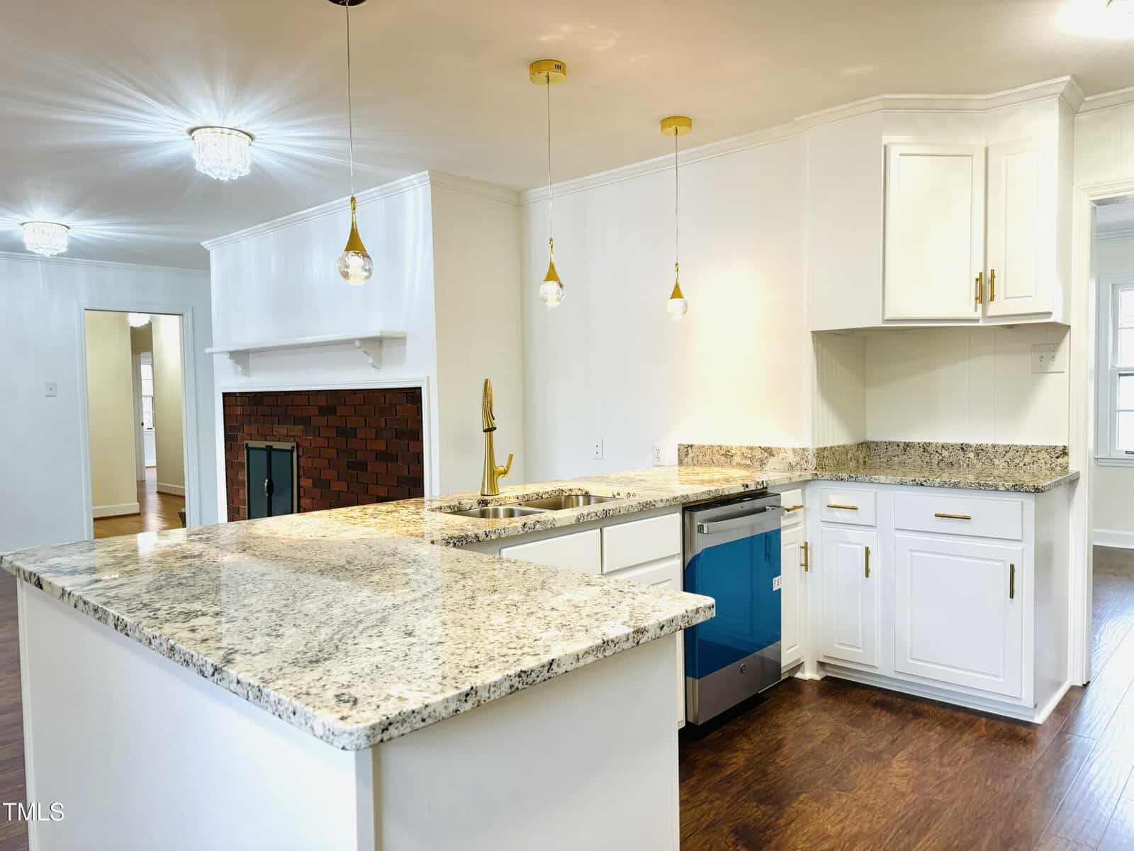 Modern kitchen interior featuring white cabinetry, granite countertops, and a bold blue oven with gold pendant lighting and a brick backsplash.