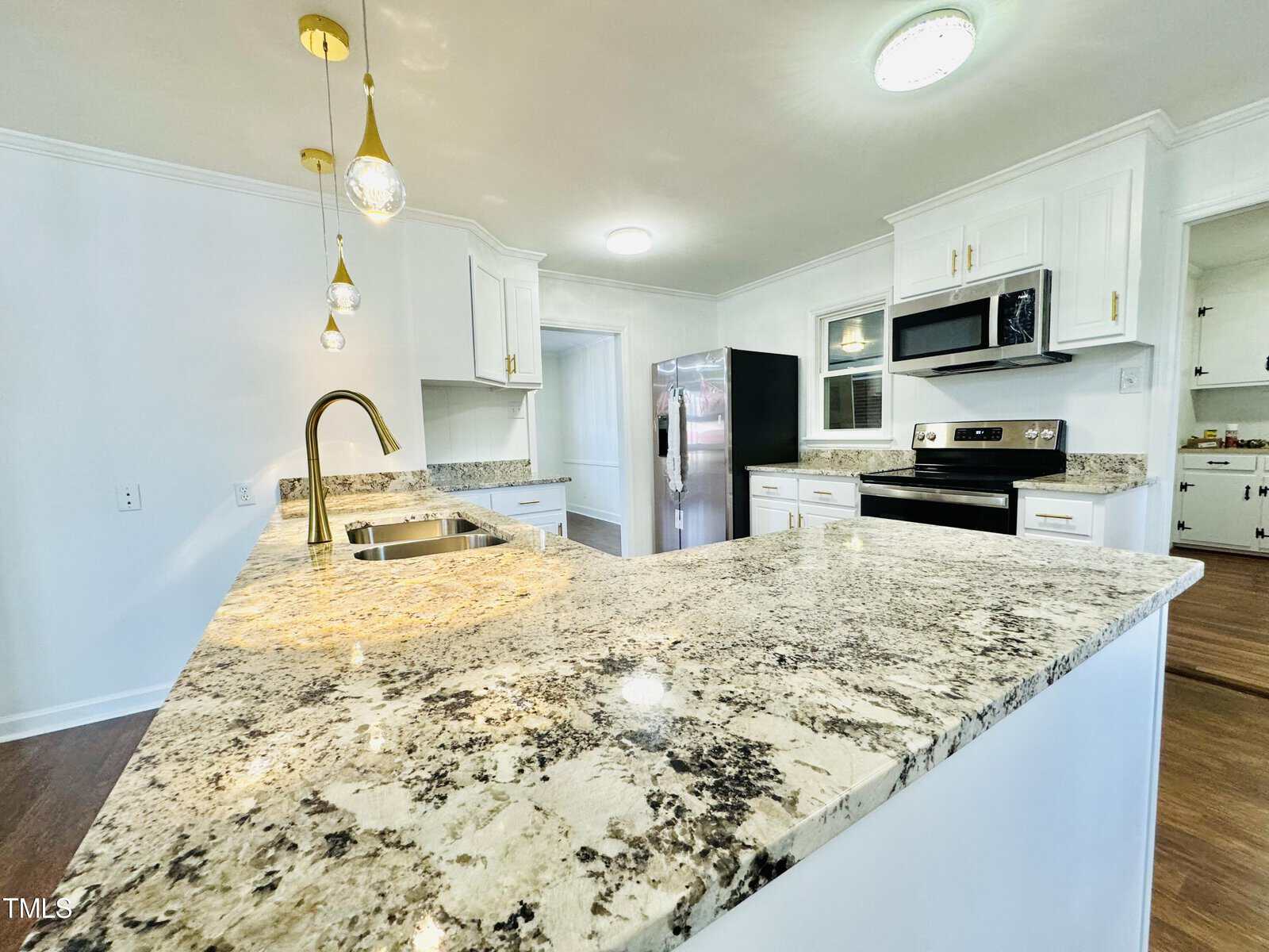 A modern kitchen with white cabinetry, granite countertops, stainless steel appliances, and a center island under pendant lights. clean and bright interior design.