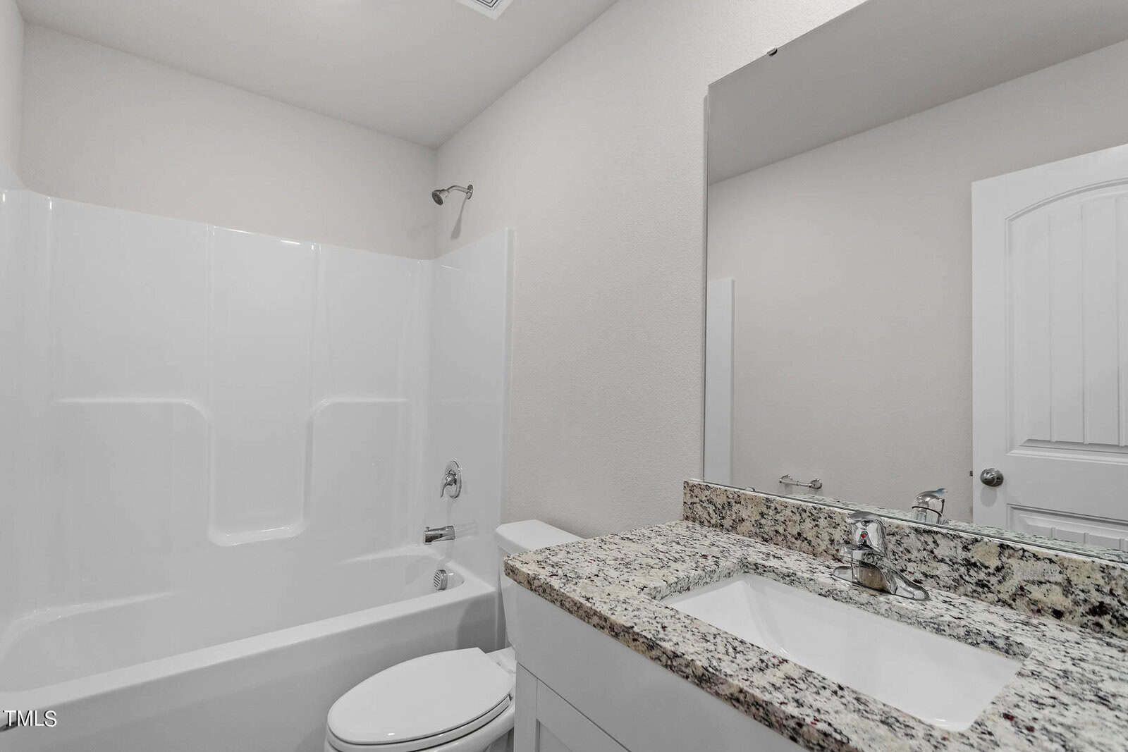 A modern bathroom featuring a white bathtub with a showerhead, a toilet, and a sink with a granite countertop. A large wall mirror is mounted above the sink. The room is well-lit with a neutral color scheme.