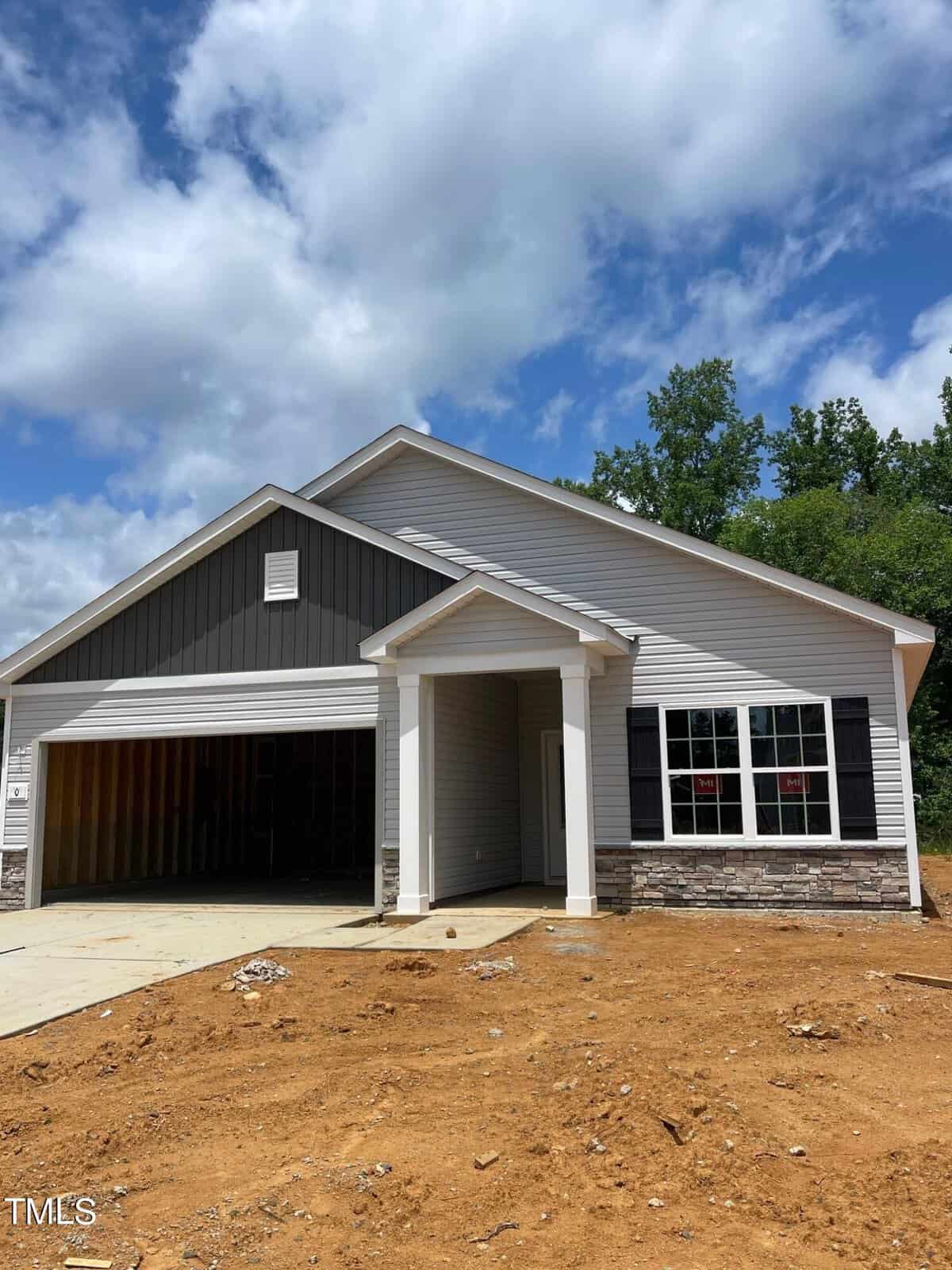 Located at 606 Rhino Bend in Oxford, this newly constructed single-story house boasts a gable roof and white siding with dark gray accents. It features a covered front entry, double garage, and a bare soil yard set against a backdrop of trees under a partly cloudy sky.