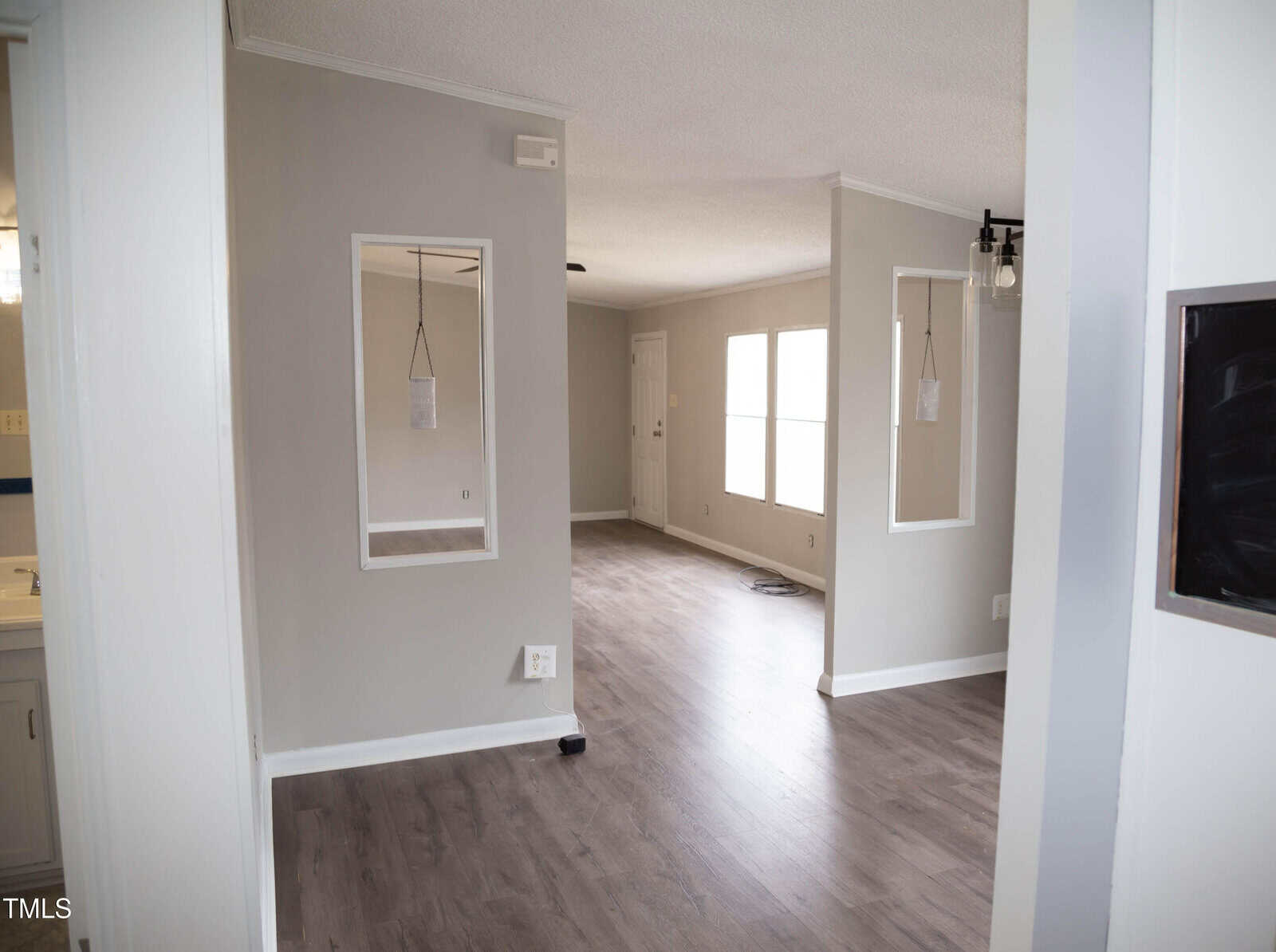 Interior of a modern house featuring clean, light gray walls, laminated flooring, and multiple doorways leading to different rooms. a framed rectangular mirror hangs on one wall.