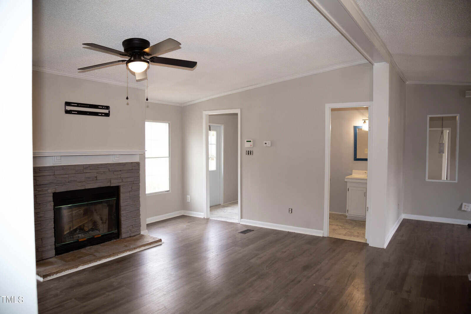 Interior of a modern living room featuring a fireplace with a white mantel, gray walls, dark wood flooring, and a ceiling fan. there are two doorways leading to other rooms.