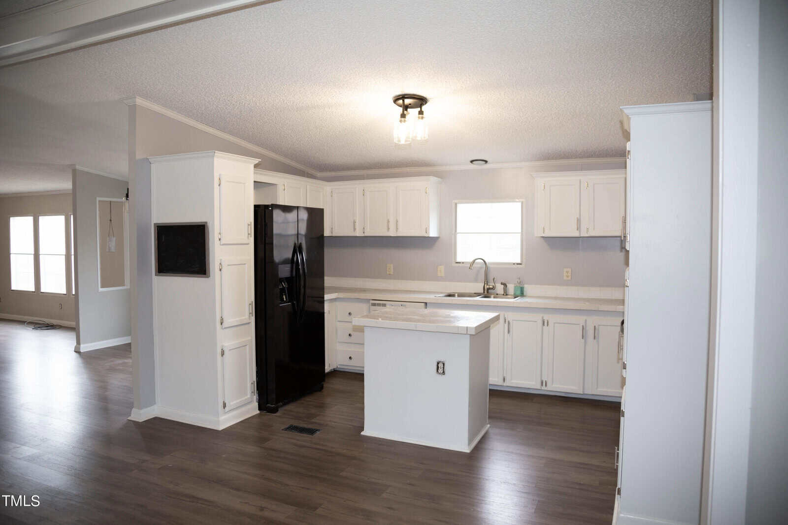 A spacious kitchen with white cabinets and a central island, featuring modern appliances, including a black refrigerator, under a ceiling with recessed lighting.