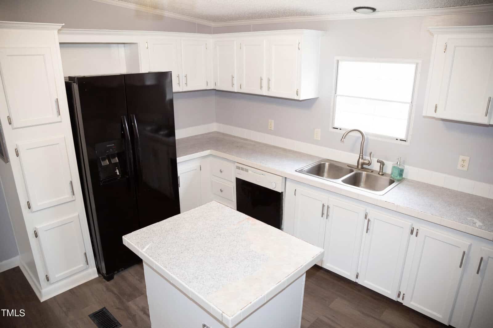 A modern kitchen with white cabinets, granite countertops, and a central island. appliances include a black refrigerator and a built-in dishwasher. there's a window above the sink.