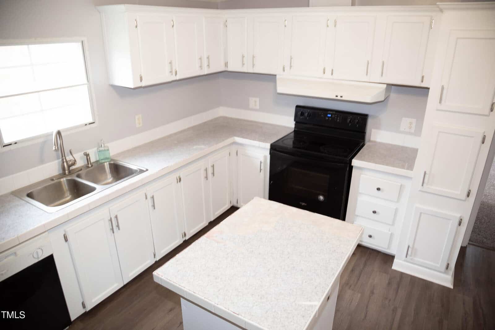 A modern kitchen with white cabinets, granite countertops, and black appliances, including a stove and dishwasher. there is a movable island in the center of the kitchen.