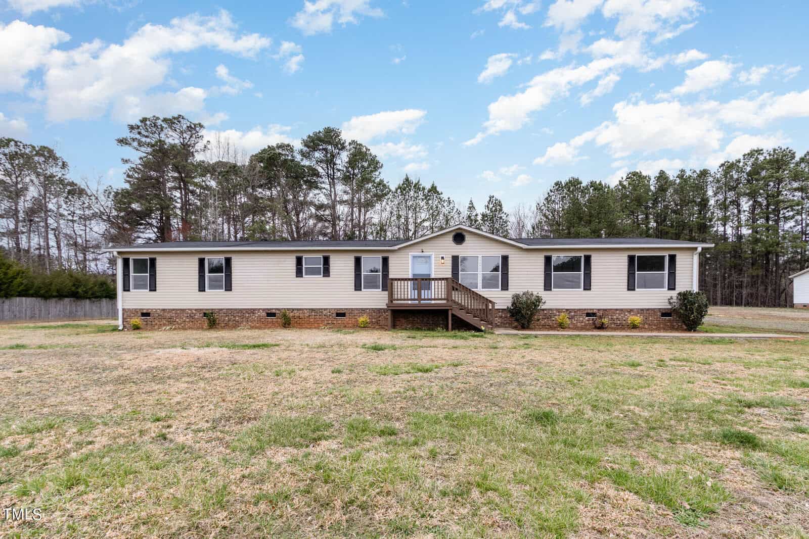 A single-story house at 1183 Diamond Hills Road boasts a beige facade, white trim, and a brown roof, set on a large grassy lawn. The home features a centered entrance with steps and is surrounded by trees under a partly cloudy sky, embodying the stem of serene suburban life.