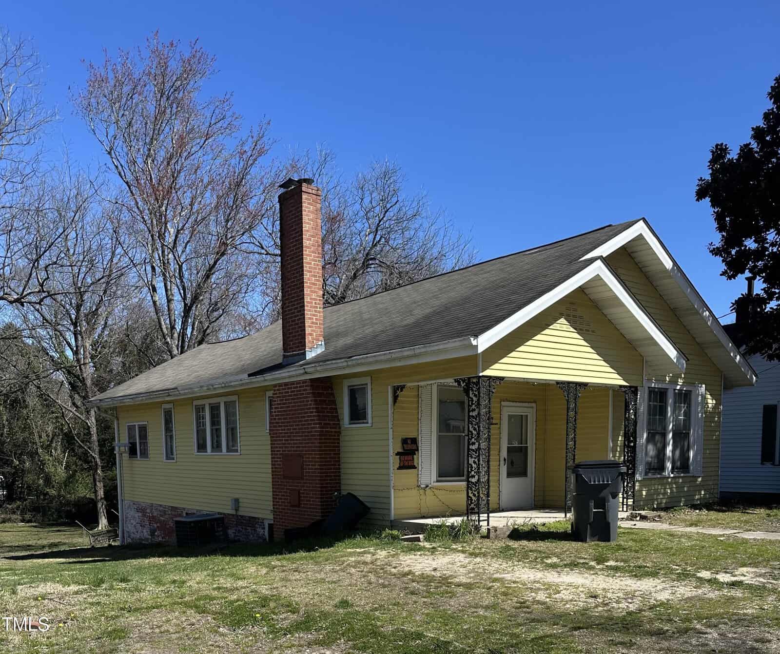 A single-story yellow house with a red brick chimney and a partially brick façade under a clear blue sky, located at 267 Chavasse Avenue in Henderson, NC.