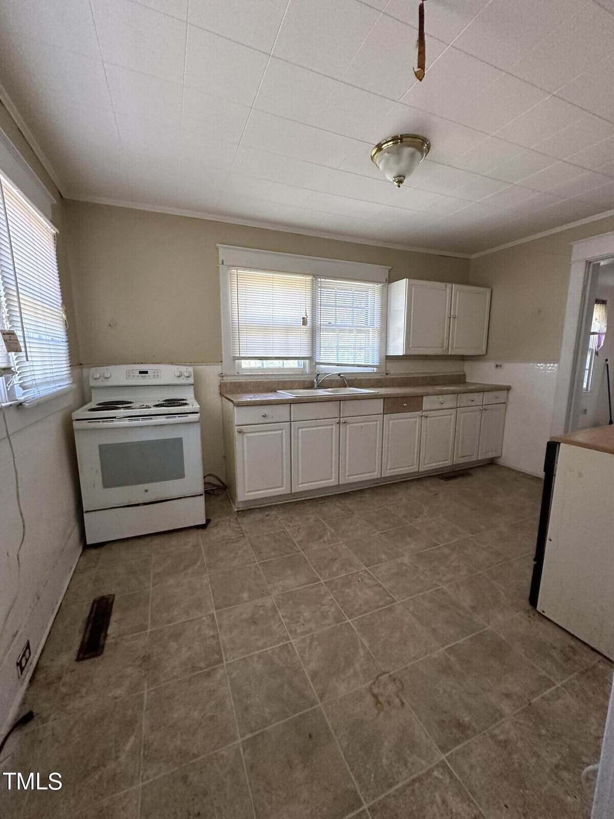 A dated kitchen interior with white cabinetry, tiled flooring, an electric range, and a window above the sink.