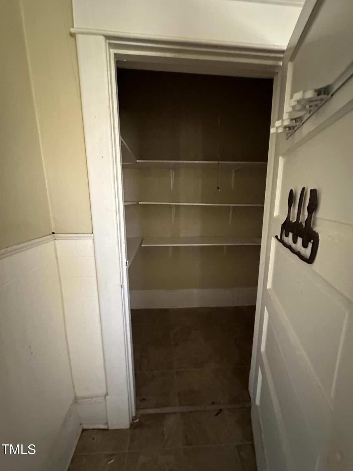 Empty walk-in storage closet with built-in shelving and tile flooring.