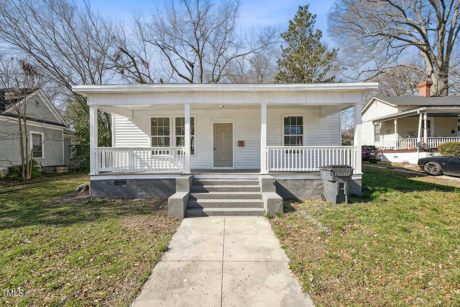 A small, white single-story house at 143 Burwell Avenue, Henderson NC, with a covered porch and three steps leading up to the front door. The house is surrounded by bare trees and similar