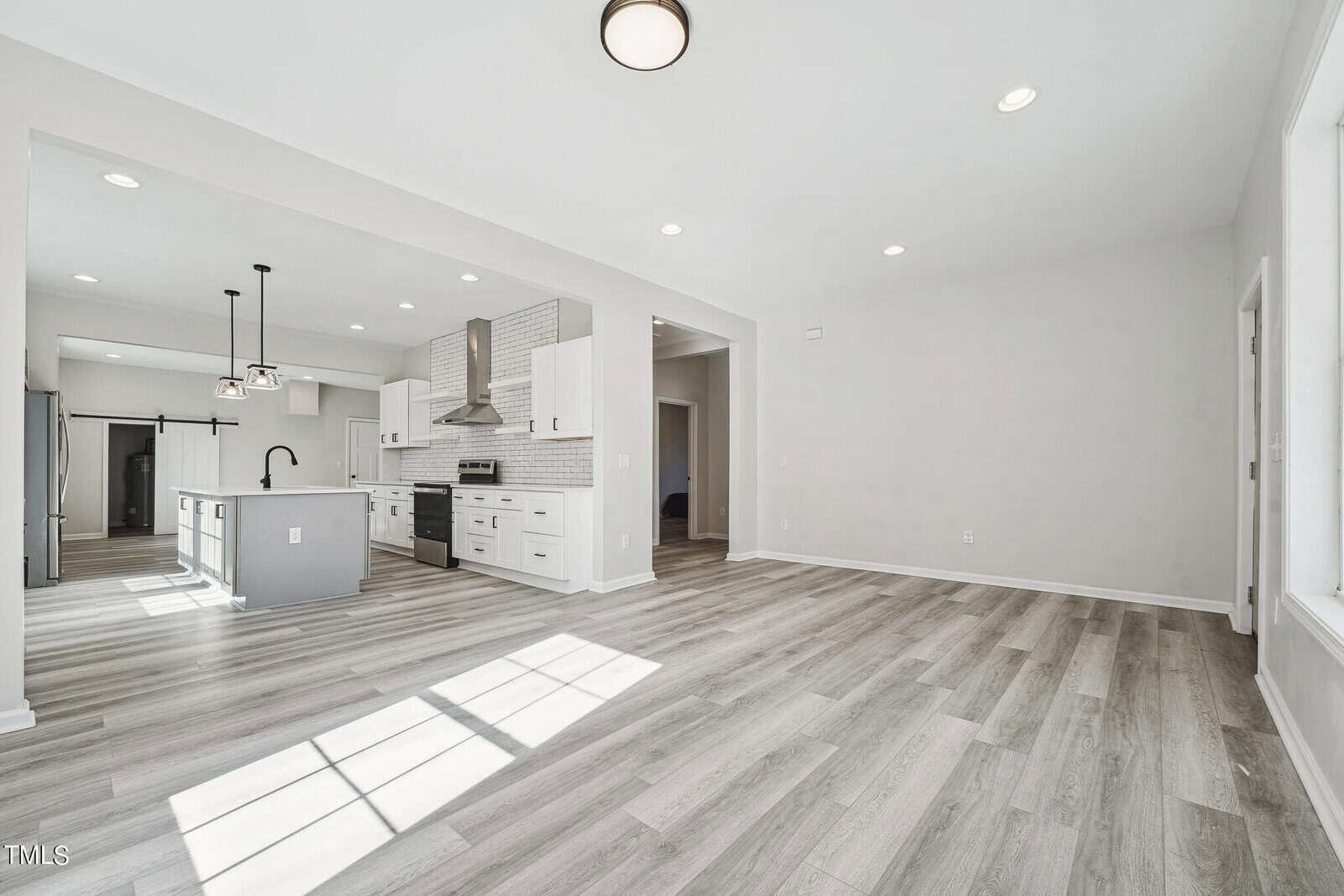 Modern kitchen with white cabinetry and grey laminate flooring. features include a central island with a sink, stainless steel appliances, and pendant lights. open concept layout with spacious ambiance.