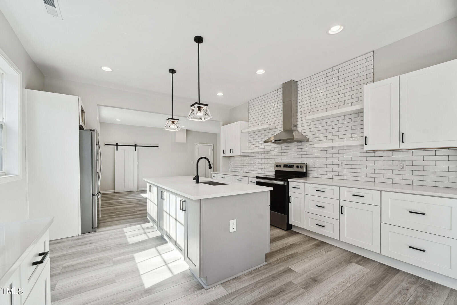 A modern kitchen with white cabinetry, stainless steel appliances, a central island, and pendant lighting, featuring a white subway tile backsplash and light wood flooring.