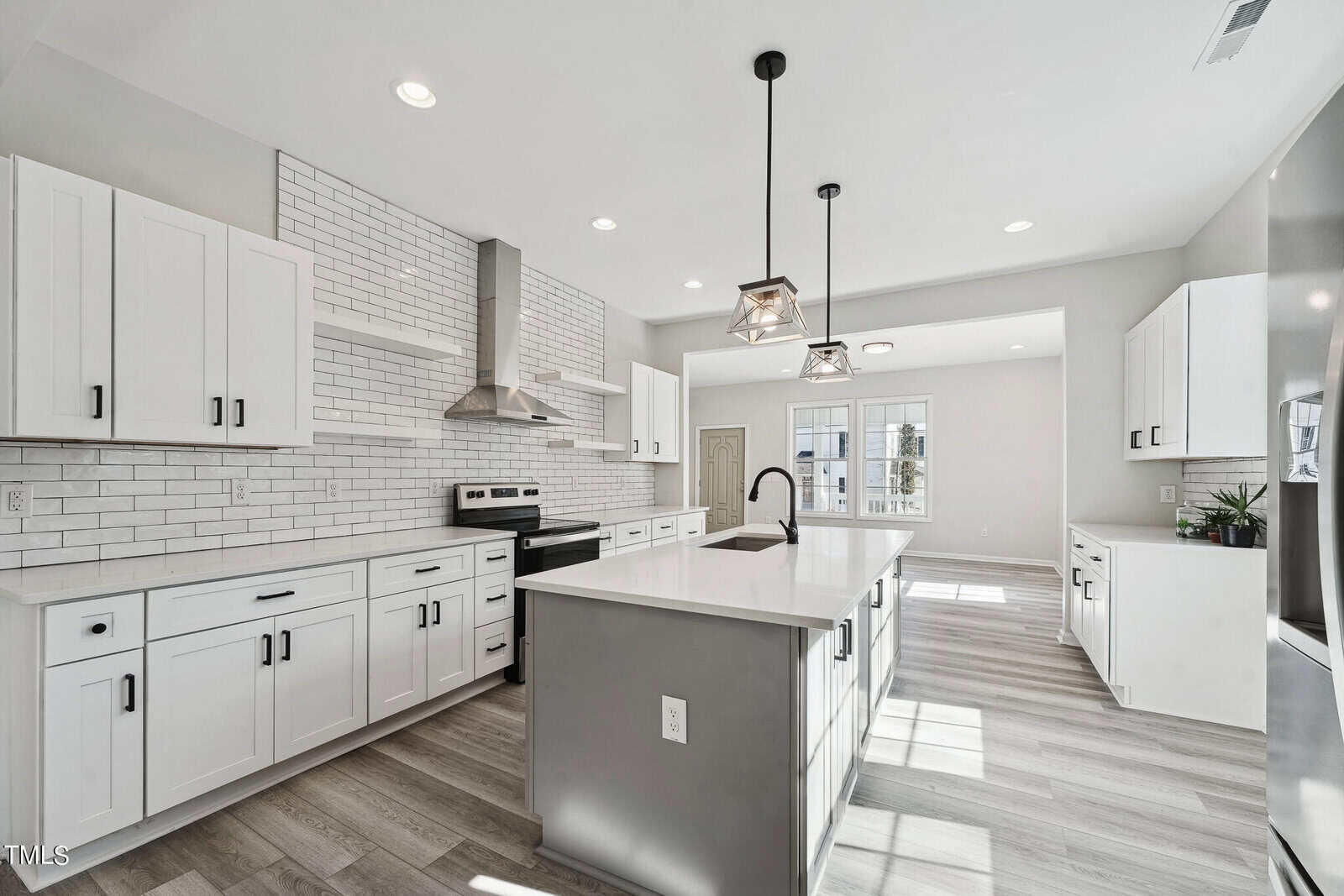 A modern kitchen with white cabinets, stainless steel appliances, a central island, and pendant lights against a subway tile backsplash. bright natural light fills the room.