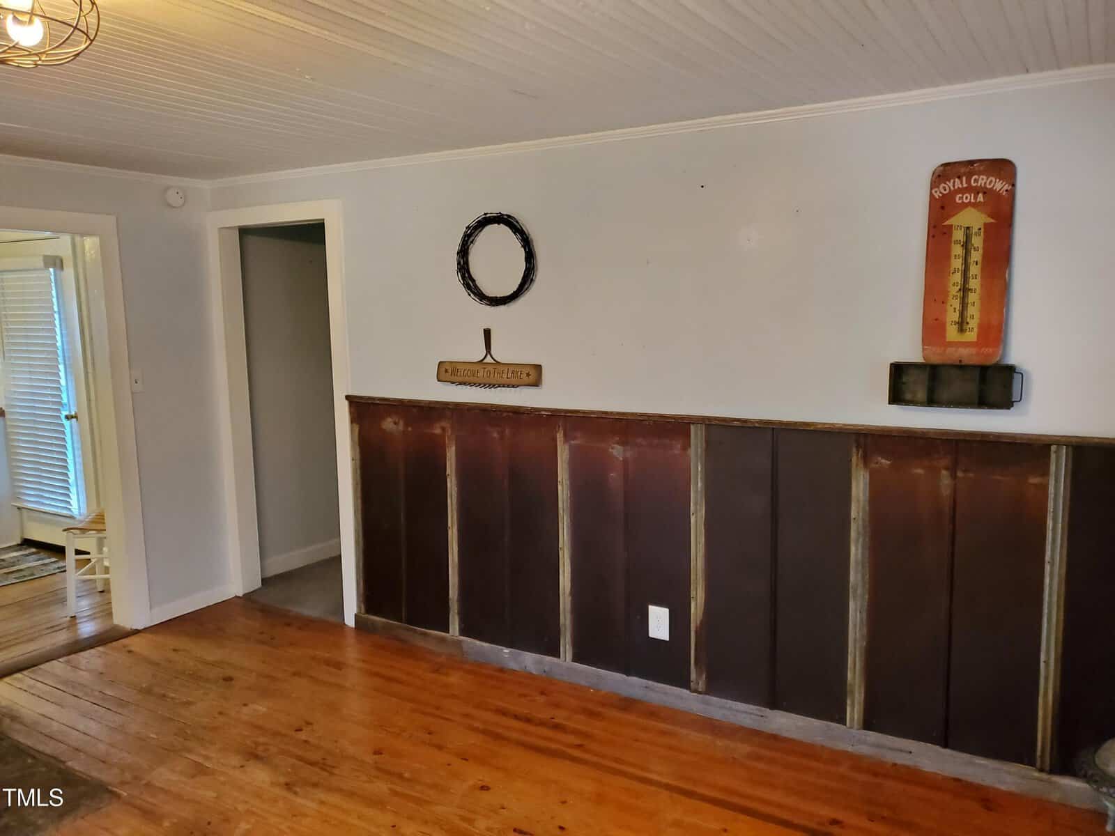 Interior of a room featuring a dark wooden half-wall paneling, hardwood floors, and light-colored walls. a decorative wreath sits on the paneling and a vintage coca-cola thermometer hangs on the wall.