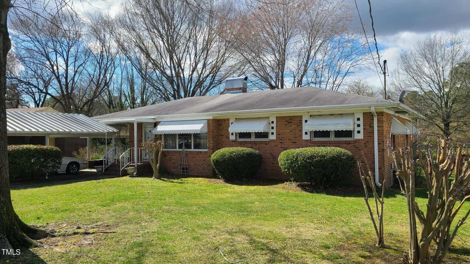 A single-story brick house at 433 Sunnyview Road, Henderson NC, with white trim and a large front yard. The house features a covered carport on the left and a bare tree in the