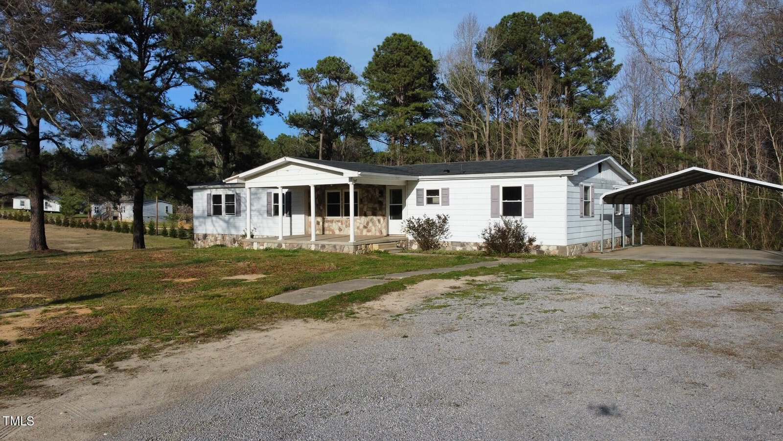 A single-story white house at 230 Finch Road, Henderson NC, with a covered porch and an attached carport, surrounded by a grassy yard and scattered trees under a clear sky.