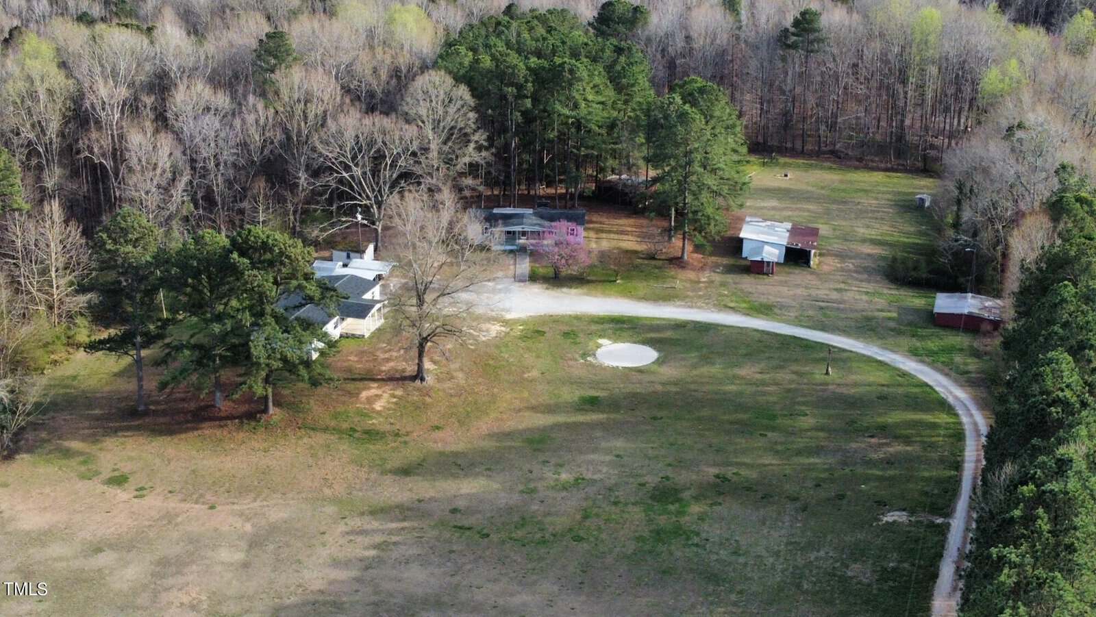 Aerial view of a rural landscape featuring a winding driveway leading to a cluster of small buildings surrounded by patches of trees and open grassy areas.