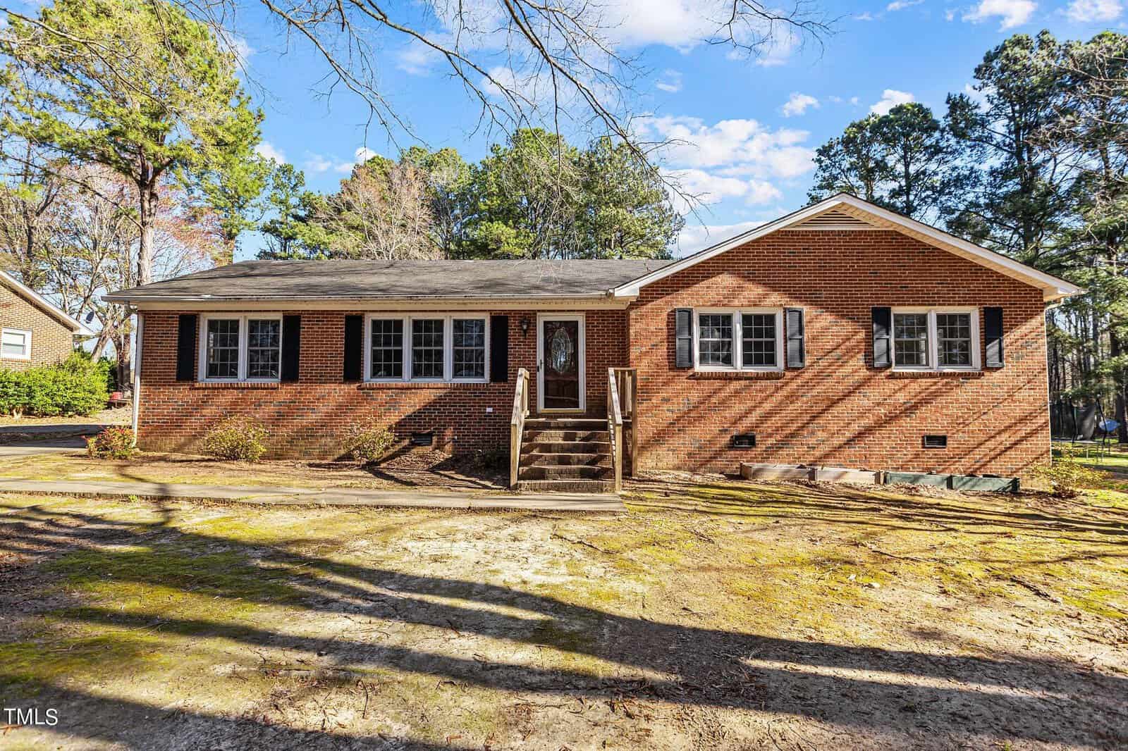 A single-story brick house on 111 Robin Road, with white-trimmed windows and a central front door. Steps lead to the entrance, set in a yard and surrounded by trees beneath a blue Oxford sky.