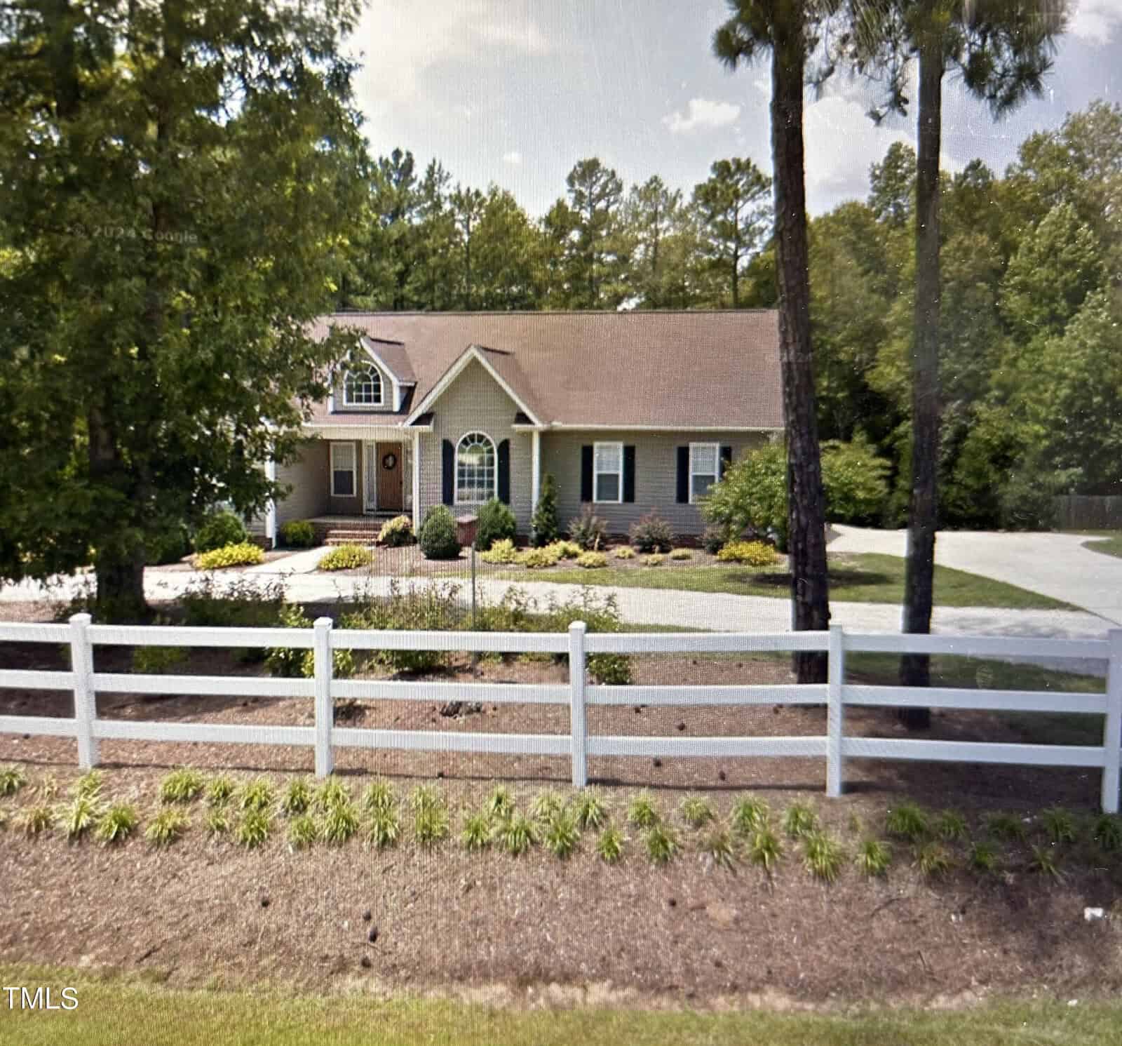 Located at 3568 Graham Sherron Road in Wake Forest, this charming single-story house features a sloped roof and is framed by lush trees. A white fence graces the foreground, complementing the neat landscape of shrubs and a driveway. The home has a central entrance topped by a small window.
