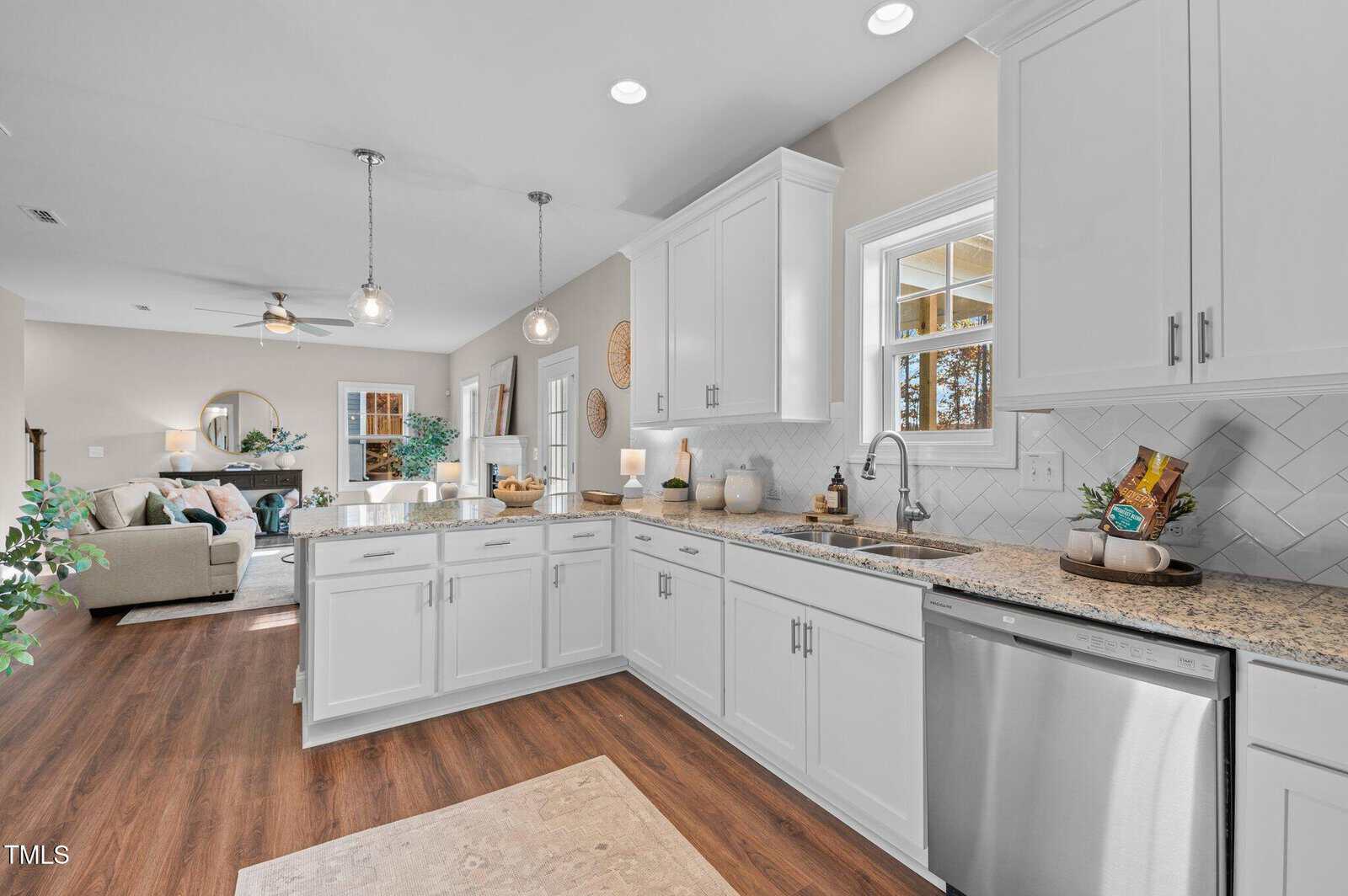 Bright, modern kitchen with white cabinets, granite countertops, stainless steel dishwasher, and wood flooring, open to a cozy living room with neutral decor and large windows letting in natural light.