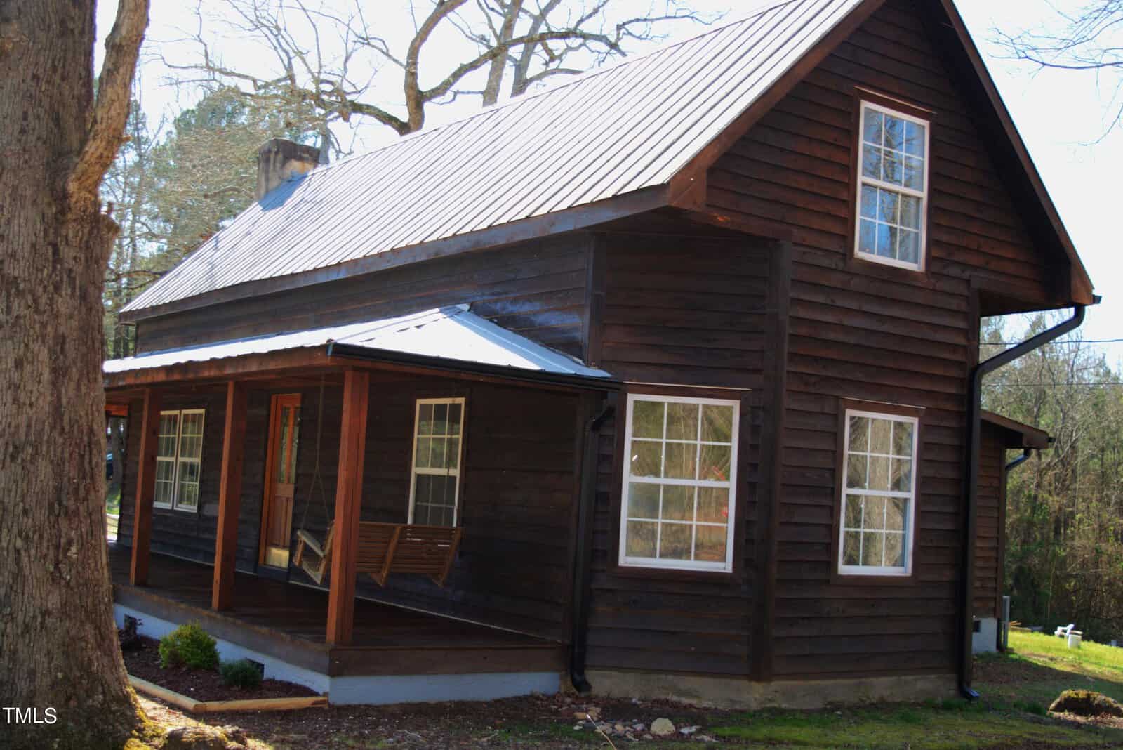 A rustic wooden cabin with a tin roof, front porch, and swing. The cabin is surrounded by trees and bathed in sunlight, creating a peaceful, secluded atmosphere.