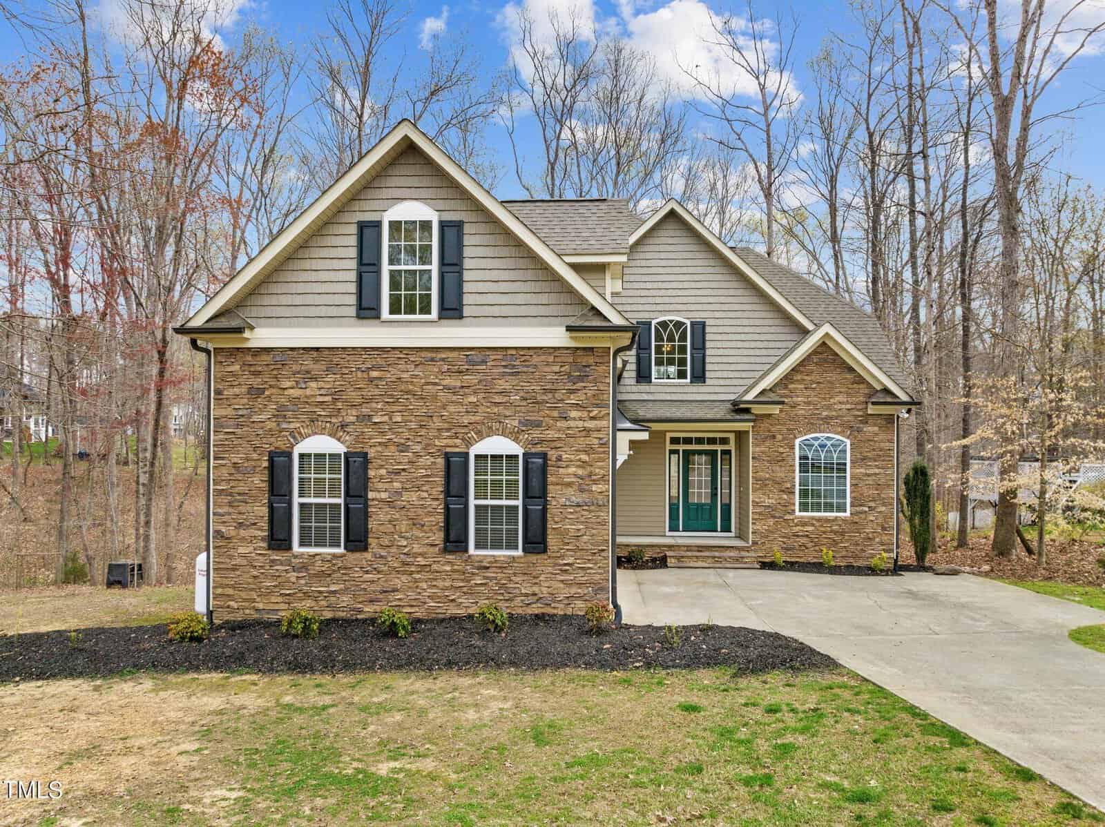 Located at 3564 Saddle Ridge Road, this two-story house boasts a stone and siding exterior with a charming covered porch and garage. Surrounded by leafless trees under a partly cloudy sky, the home's welcoming driveway seamlessly guides you to its entrance.