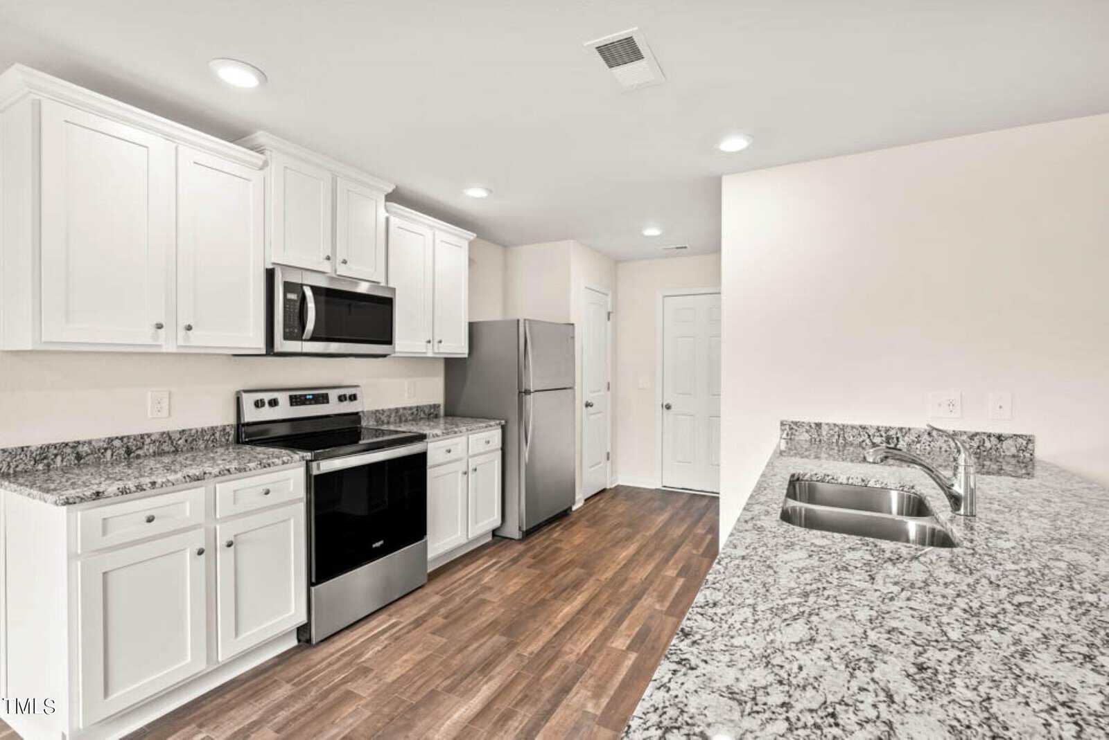 Modern kitchen with white cabinets, stainless steel appliances, and granite countertops. Includes a refrigerator, oven, and microwave. Hardwood floors and bright lighting complete the sleek design.