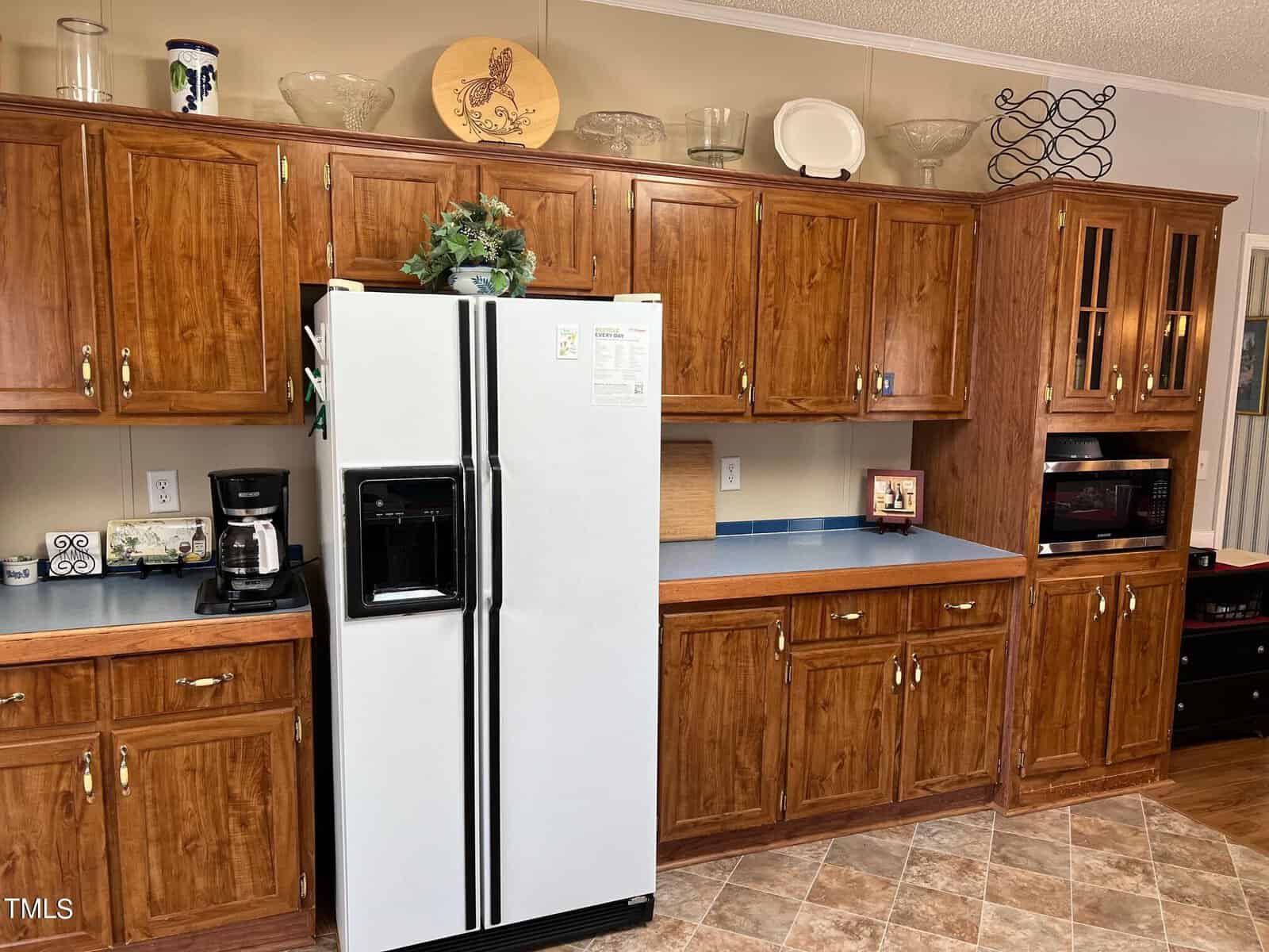 A well-organized kitchen with wooden cabinetry, a white side-by-side refrigerator, and black appliances including a microwave and oven. decorative items are displayed above the cabinets.