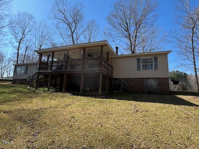 A two-story house with a large deck, set on a grassy hill with bare trees in the background under a clear blue sky.