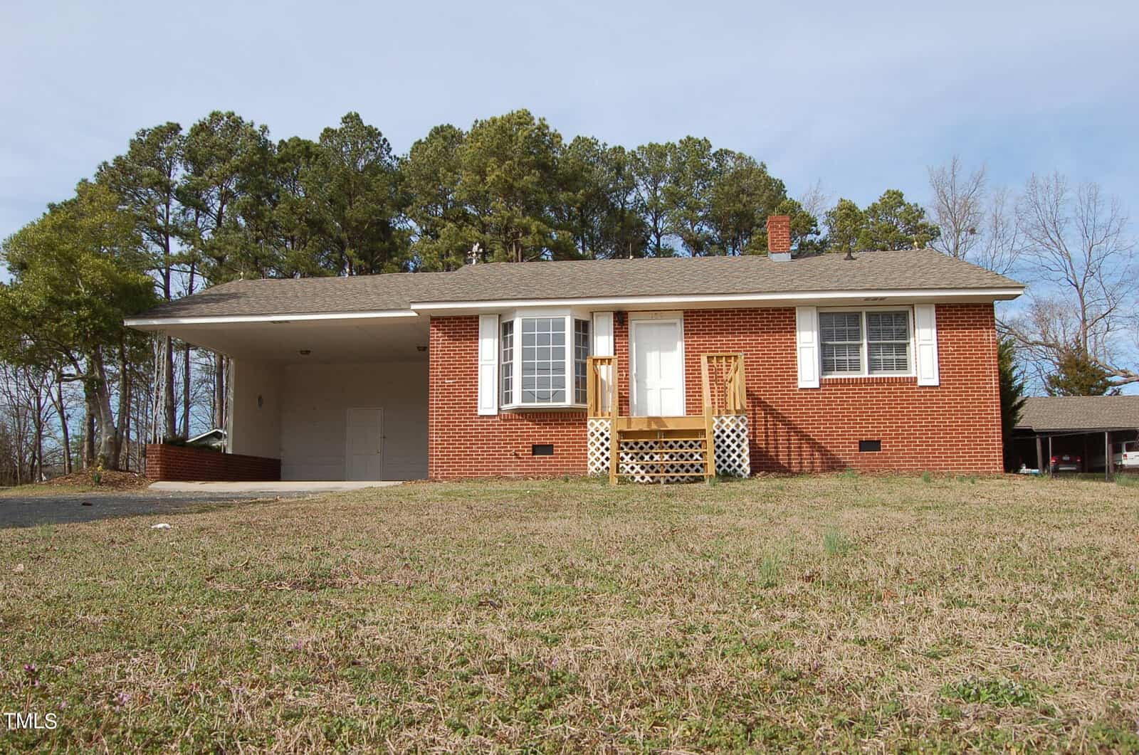 A single-story brick house on 109 Moss Road features a small front porch, white door, and large window. There's a carport on the left side and a grassy front yard. Nestled in Creedmoor, trees are visible in the background under a clear sky.