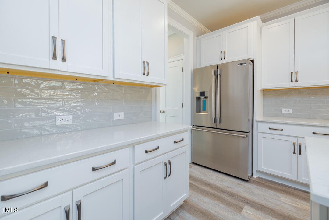 Modern kitchen interior with white cabinetry, stainless steel refrigerator, and light wood flooring.