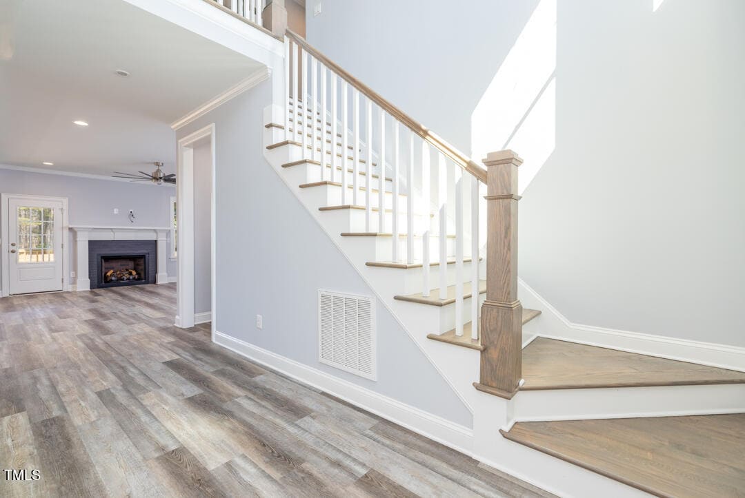 An image of a well-lit interior showing a staircase with wooden balusters and handrail, leading up from a room with hardwood flooring, with a fireplace visible in the adjacent room.