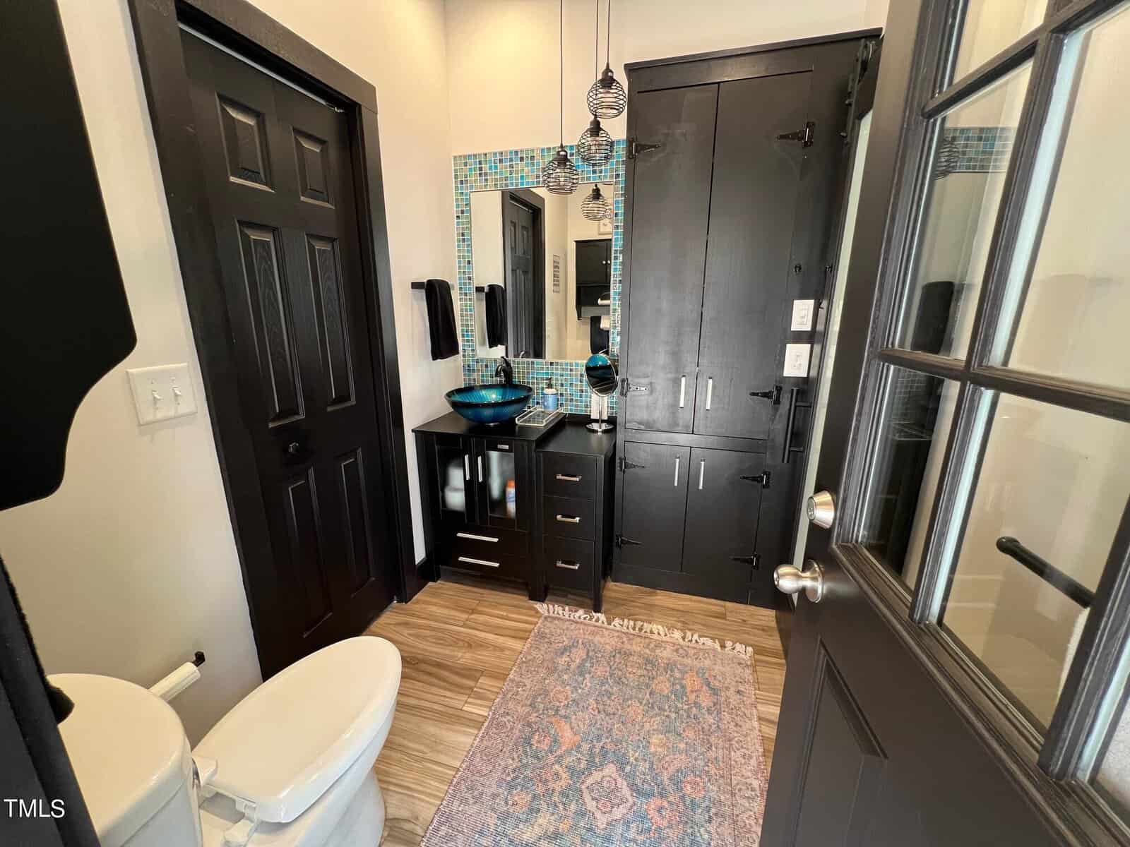 A stylish bathroom featuring black cabinetry, a turquoise backsplash, and a combination of patterned and solid rugs. the room includes modern fixtures and natural light.