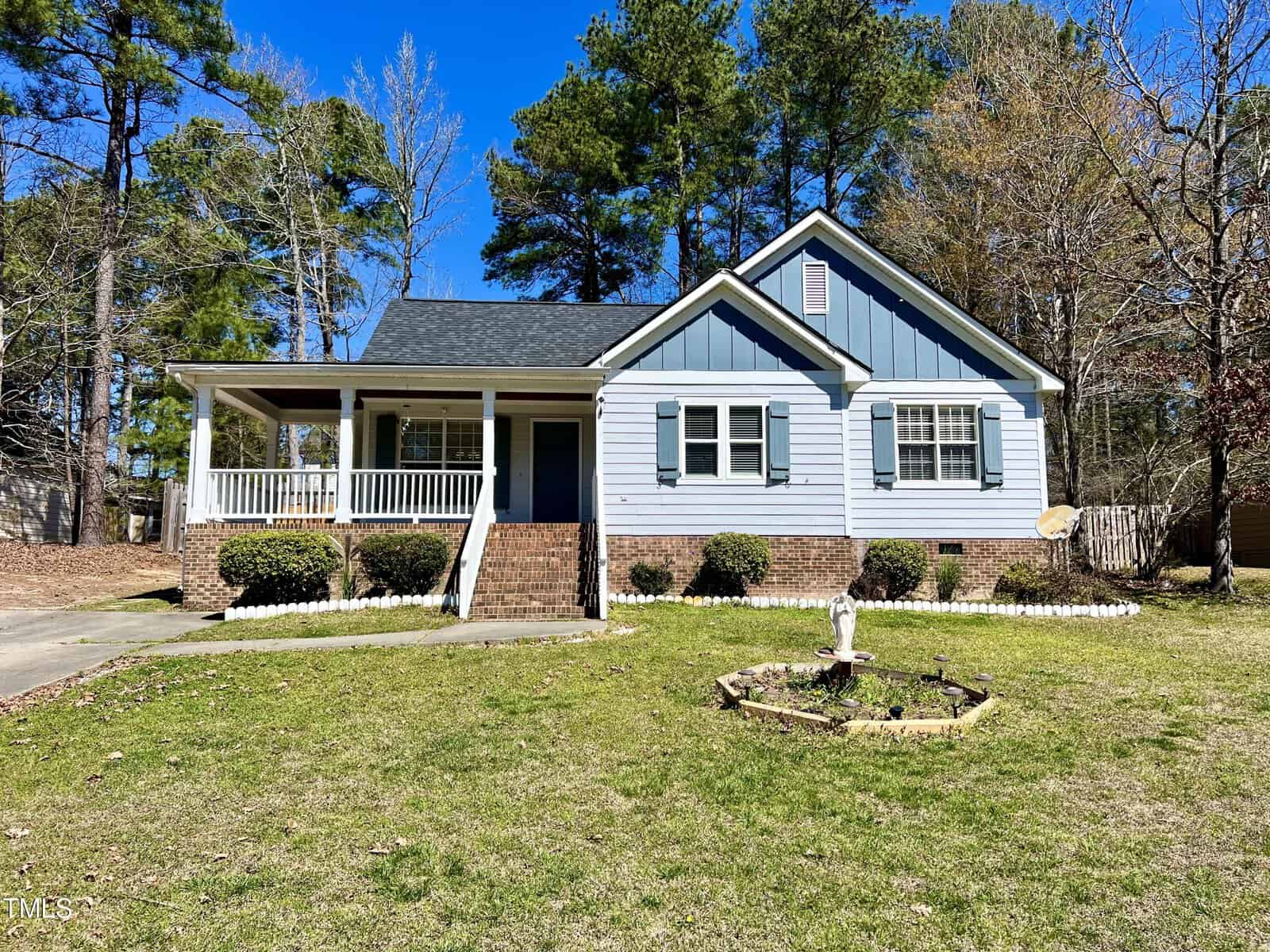Nestled on 2757 Clifton Avenue, this charming blue and white house in Creedmoor features a porch set before a lush lawn. With its brick foundation, multiple windows, and a quaint front garden complete with a bird bath, it's surrounded by tall trees beneath a clear blue sky.