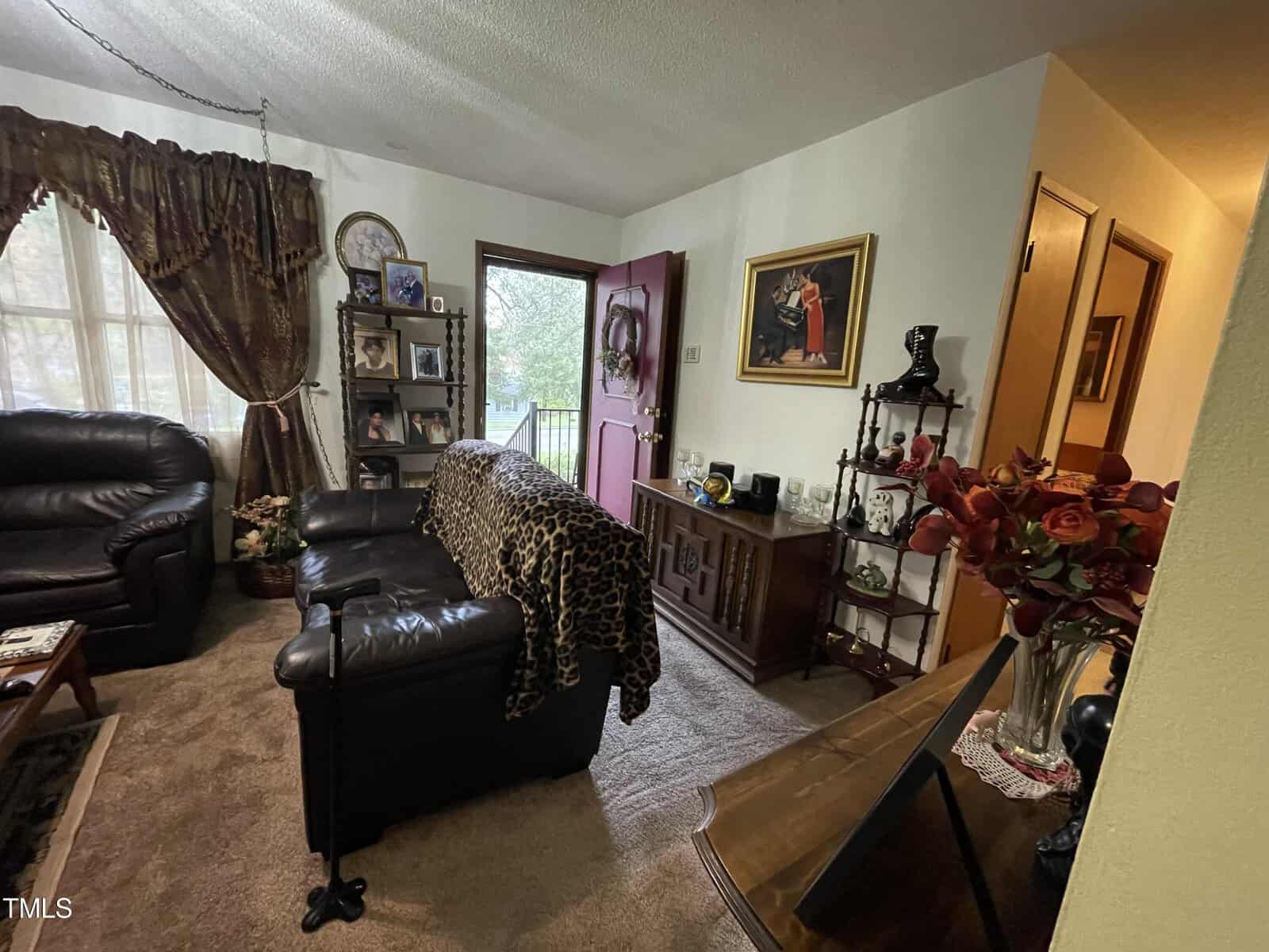 A cozy living room with a black leather sofa, a leopard print chaise lounge, and a wooden coffee table. decor includes floral arrangements, framed pictures, and a small cabinet.