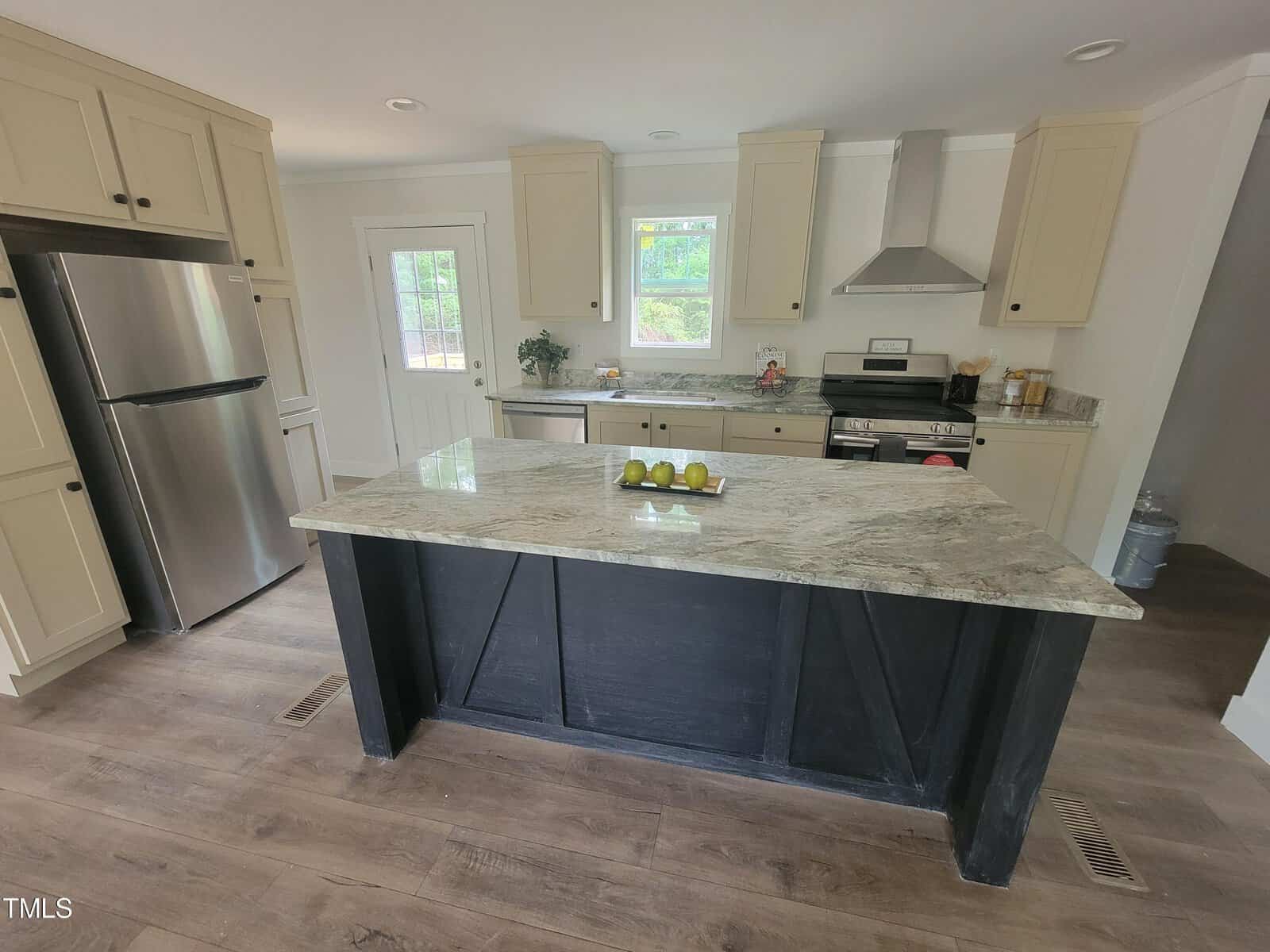 A modern kitchen with white cabinetry, stainless steel appliances, a dark kitchen island with a marble top, and wood flooring under bright natural light.