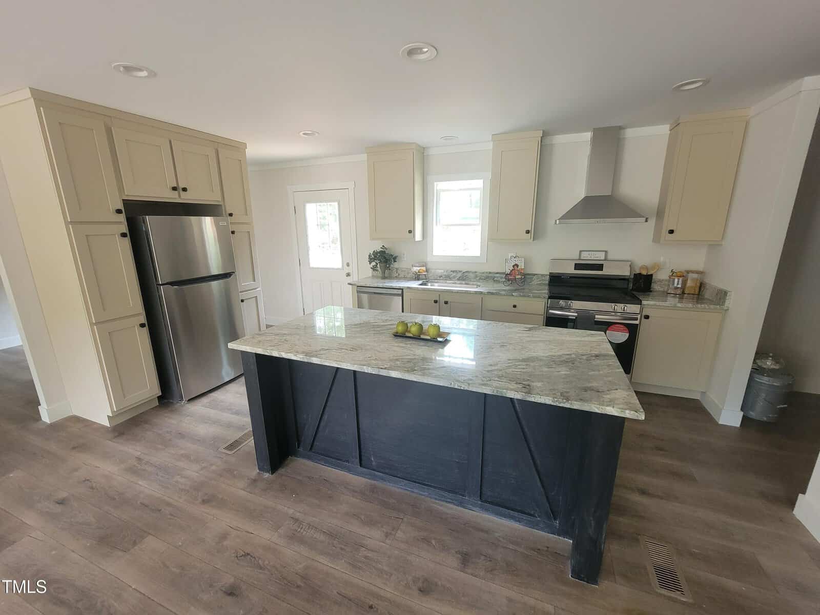 Modern kitchen with beige cabinets, stainless steel appliances, and a dark island with a granite countertop. the space features hardwood floors and recessed lighting.