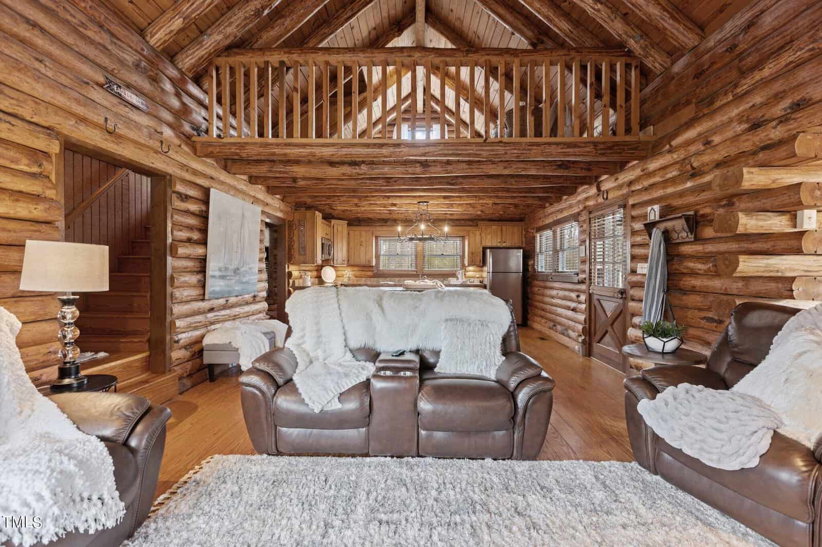 Interior of a cozy, rustic log cabin with exposed wooden beams, featuring a plush leather sofa, a fur-covered bed, and a large fluffy area rug, creating a warm and inviting atmosphere.