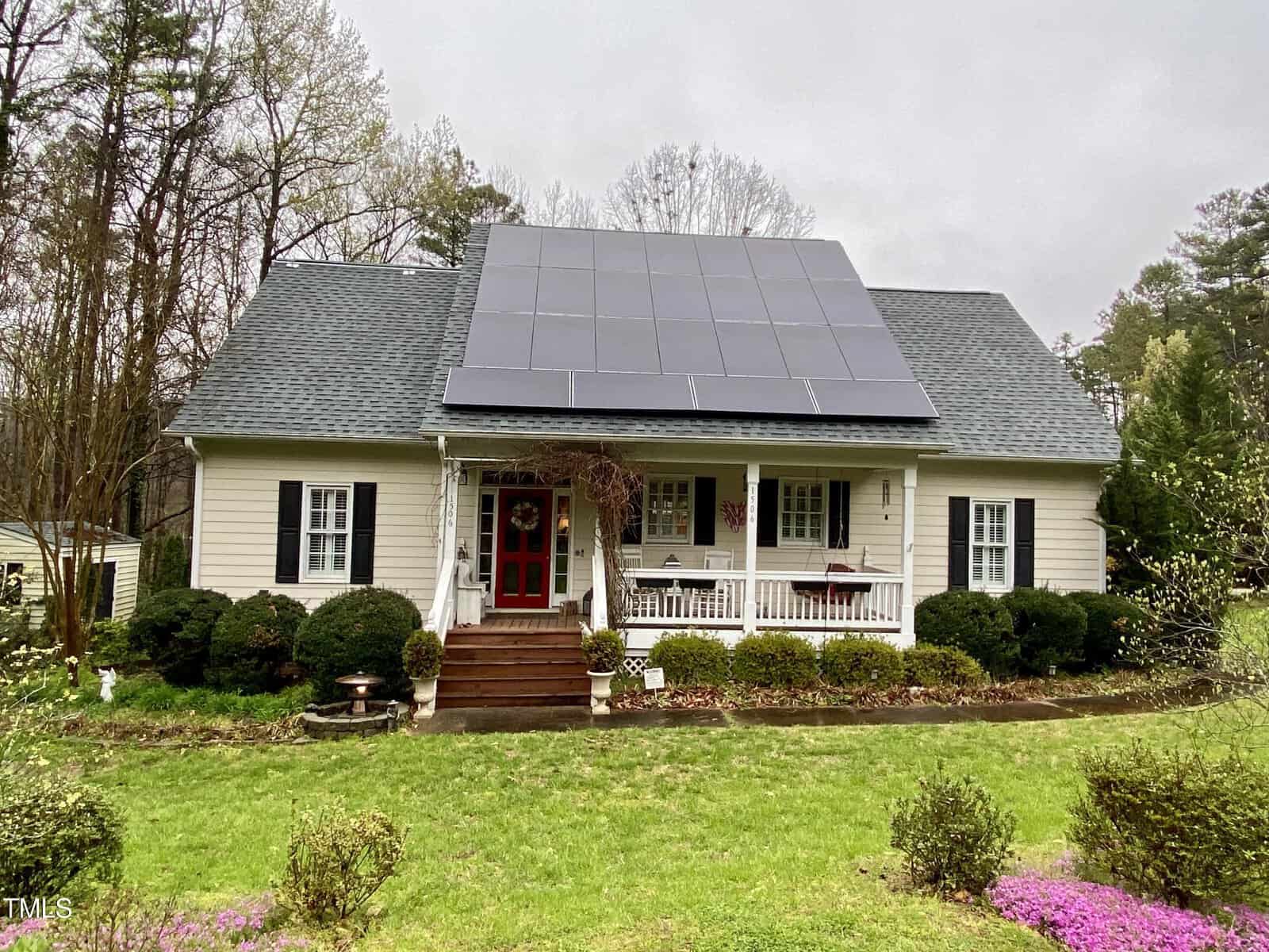 A quaint, single-story white house located at 1506 Peace Street, Henderson NC, with a large array of solar panels on the roof. The house features a front porch with a red door and