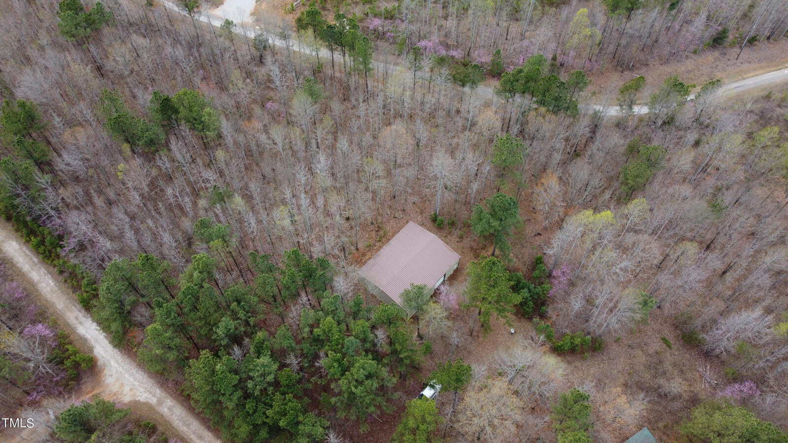 An aerial view captures a house nestled in a dense forest at 4 Rocky Ridge Road, Oxford. Surrounded by a mix of bare and evergreen trees, two dirt roads intersect at the top and right of the image, providing access to this secluded property.
