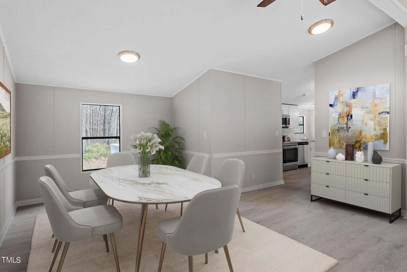 Modern dining room with a round marble table, four gray chairs, and a white cabinet, leading to an open kitchen. large windows provide a view of the exterior. decor includes subtle wall art and flowers.