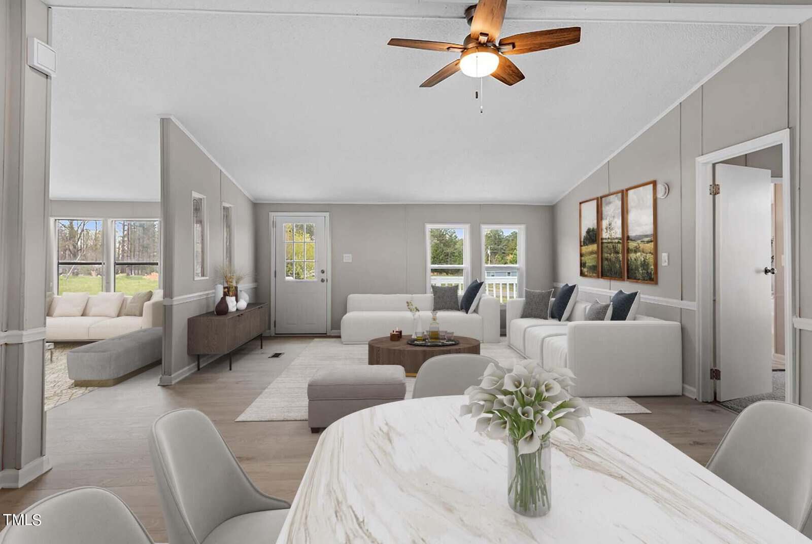 Modern, open-plan living space with neutral-tone furniture, sleek wood flooring, and bright natural light. featuring a ceiling fan, minimalist decor, and views to an outdoor garden.