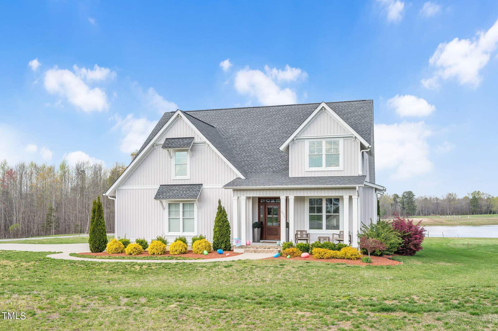 Located at 2514 Jessis Court in Franklinton, this modern two-story white house features dark roofing and a spacious lawn. The inviting front porch is adorned with chairs and framed by neatly trimmed shrubs and small trees, set against a backdrop of a partly cloudy blue sky and a serene pond.