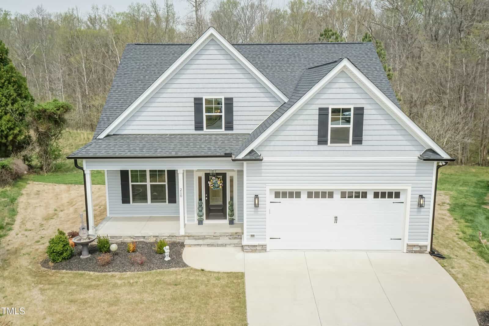 A modern two-story house at 210 Cambridge Way with gray siding, a dark roof, and a two-car garage. The front porch is decorated with a wreath on the door. Located in Oxford, the house is surrounded by a neat lawn and bordered by trees in the background.