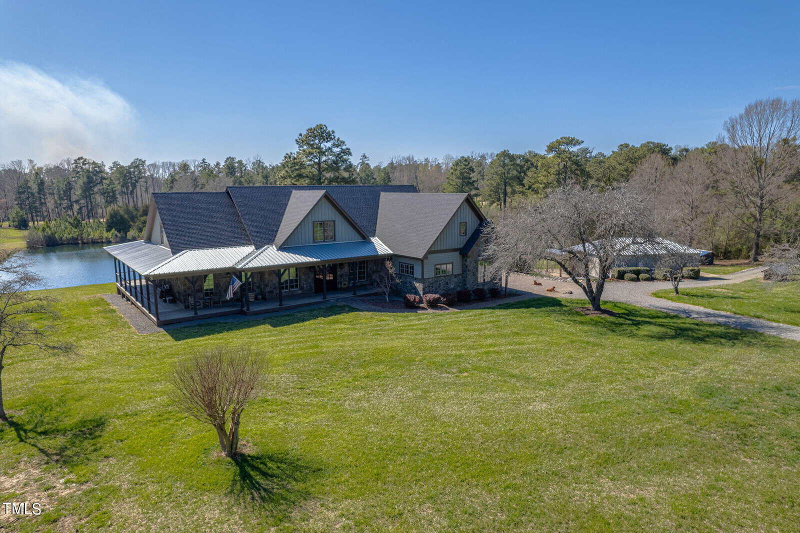 A large house with a gray roof sits on a grassy lawn beside a serene pond in Franklinton. Nearby, at 1641 State Hwy 96, stands a smaller building surrounded by trees and clear blue sky. A paved path gracefully leads to the main house.