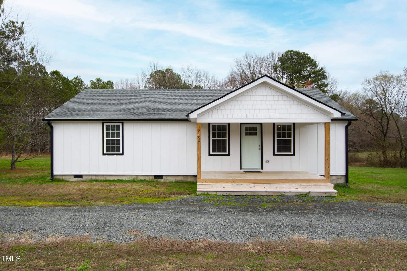 A charming white house on 3108 E Thollie Green Road boasts a gabled roof and inviting front porch. Nestled in Stem, it sits on a grassy lawn embraced by trees under a partly cloudy sky, creating a serene escape.