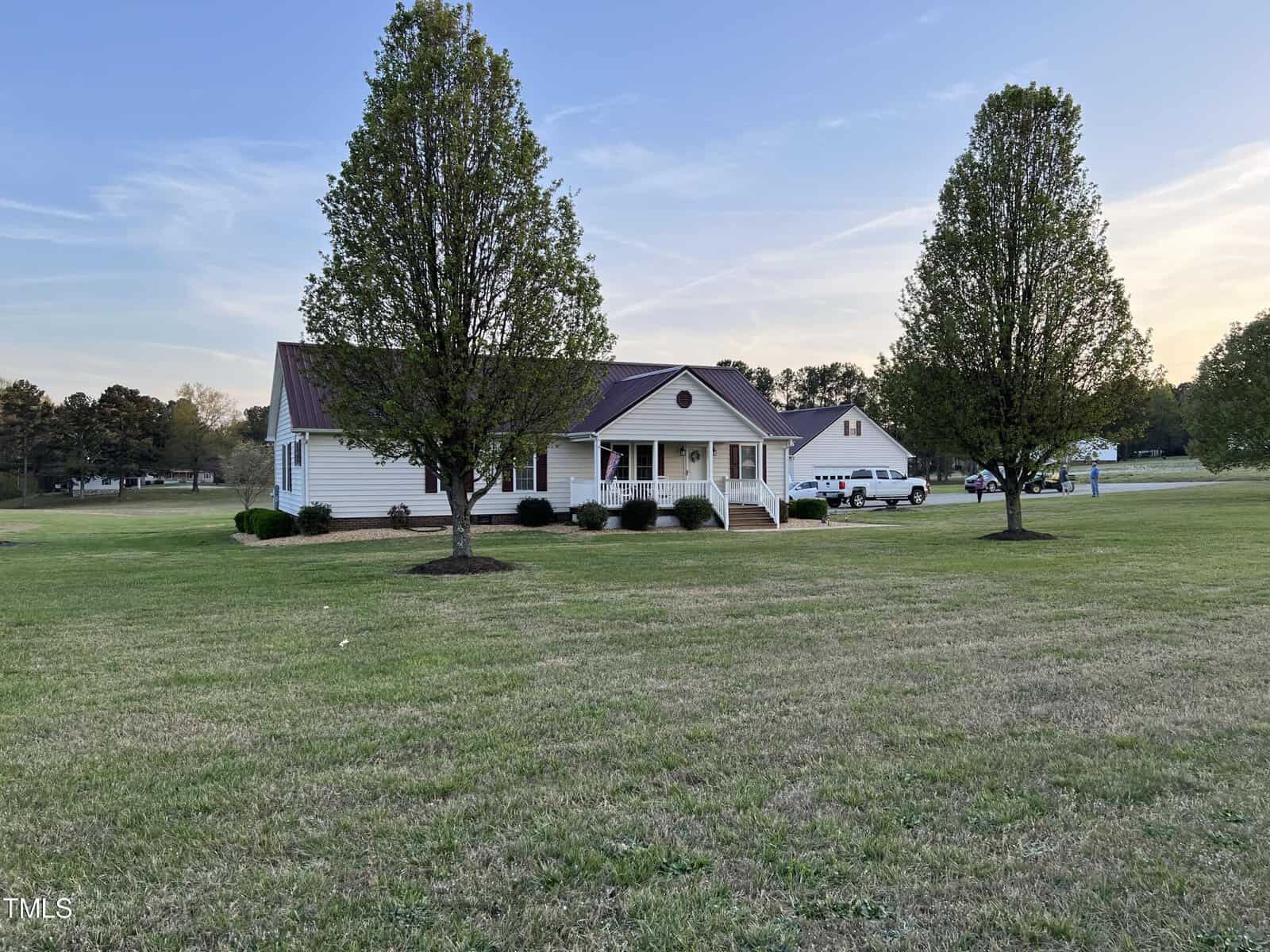 A single-story suburban house at 246 Finch Road, Henderson NC, with a red roof and white siding, featuring a front porch. Two tall trees flank the home in a large grassy lawn during