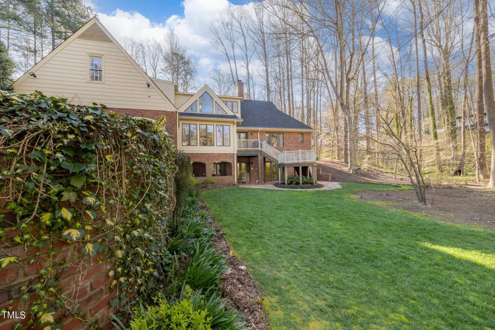 A spacious two-story house with a combination of brick and siding exterior, surrounded by tall bare trees and a well-maintained lawn, under a clear blue sky.