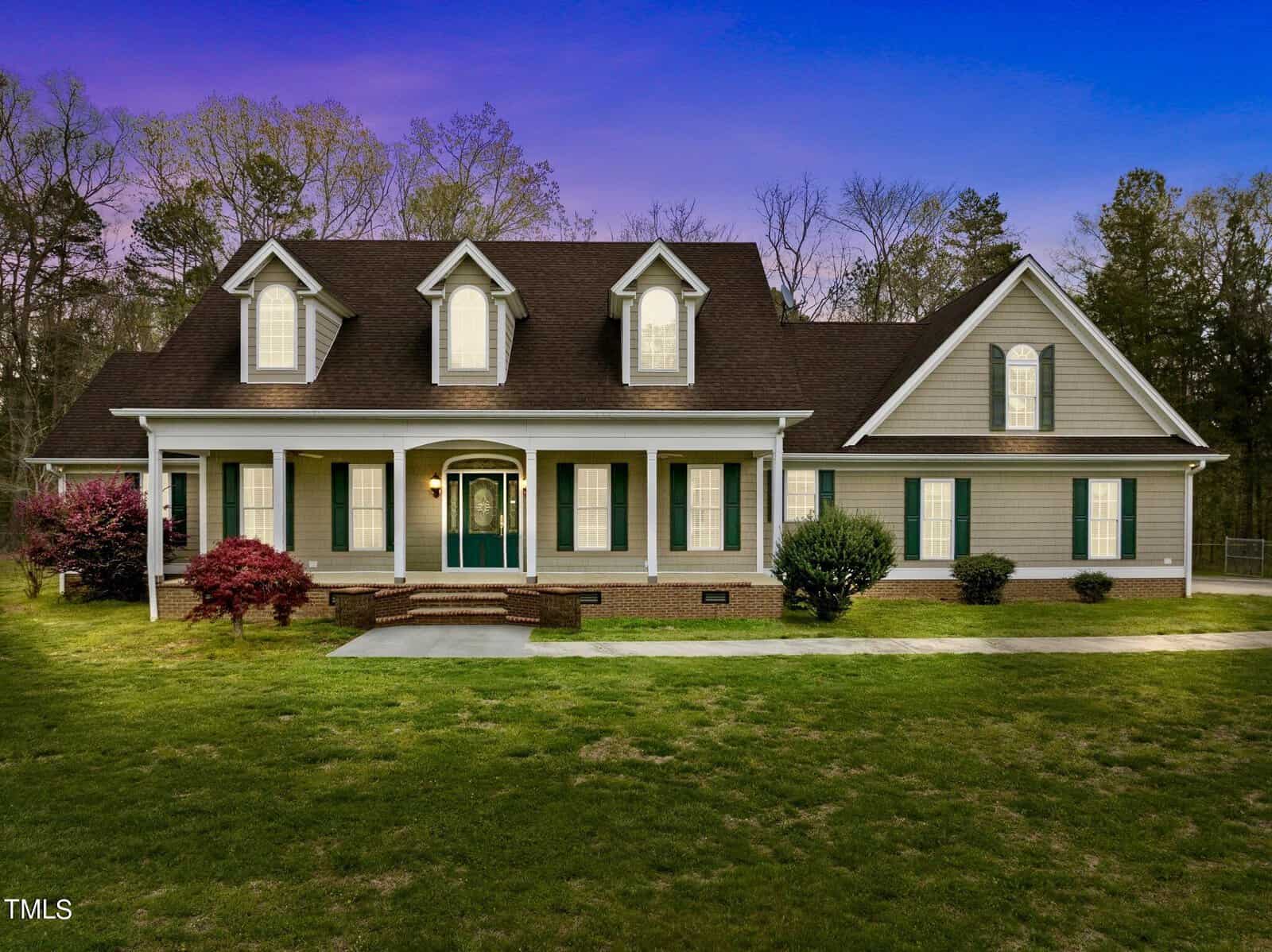 A large two-story house on 3194 Herbert Faucette Road boasts a manicured lawn, featuring a front porch, dormer windows, and a shingled roof. Surrounded by trees in Bullock, it stands gracefully beneath a vibrant sky at dusk.
